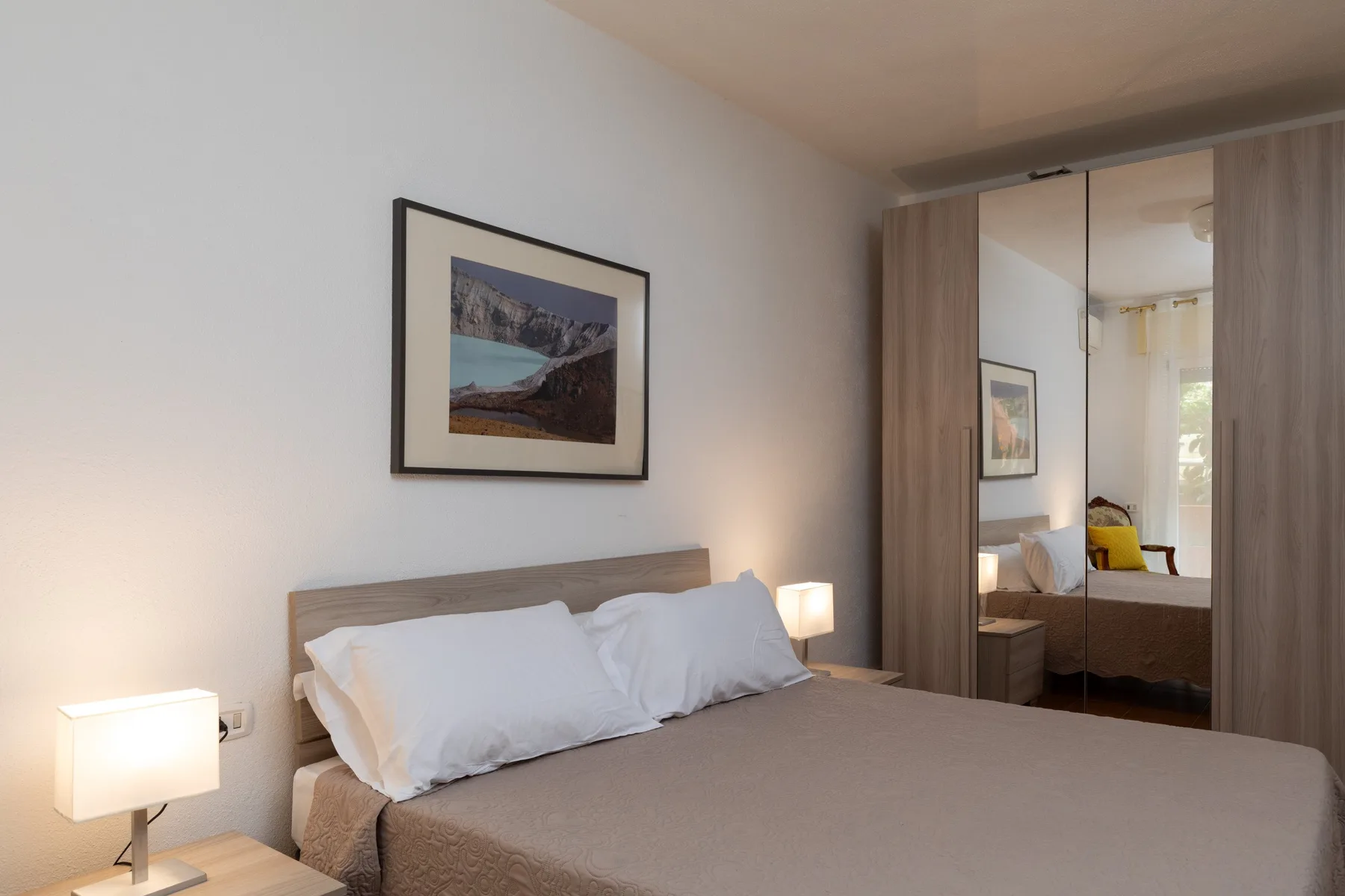 Un dormitorio con una cama ordenada y un armario con espejos.