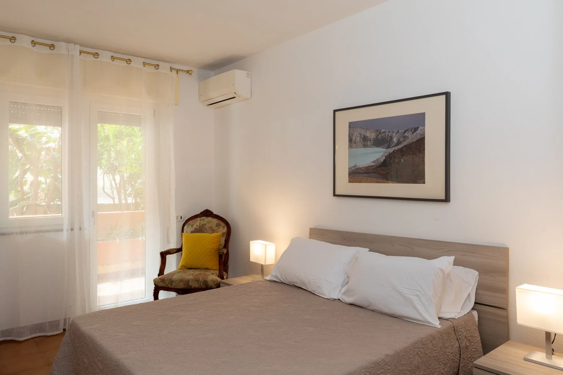 Un dormitorio con una cama, un sillón y un paisaje enmarcado.