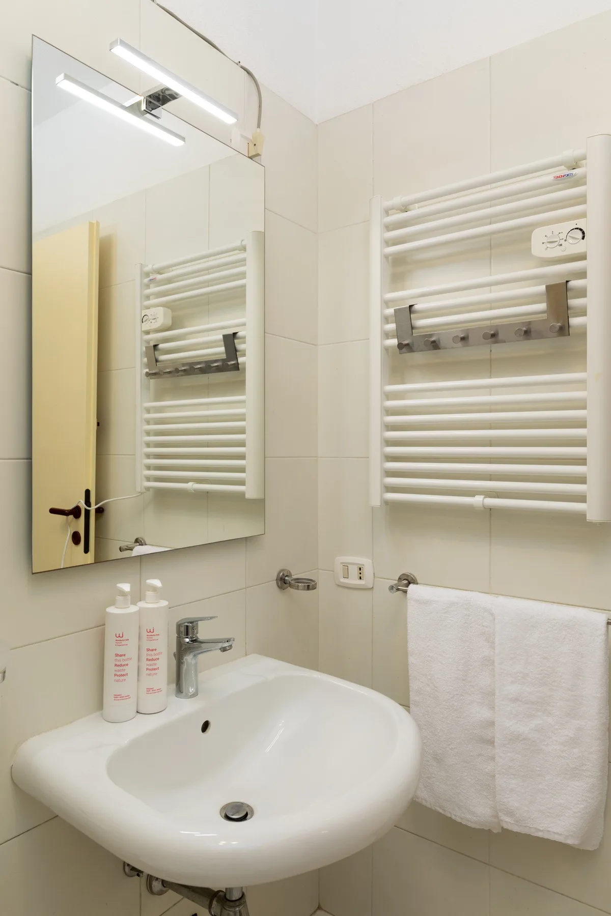 Baño alicatado con lavabo blanco, espejo y toalleros calefactores.