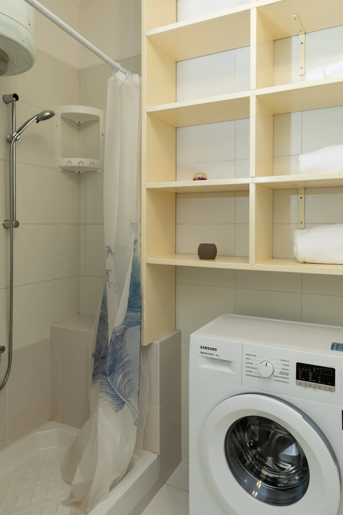Un baño con ducha, estanterías abiertas y una lavadora.