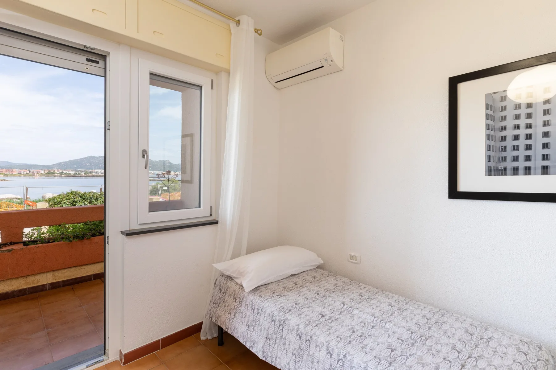 Un dormitorio con una cama individual junto a una ventana con vistas al balcón.