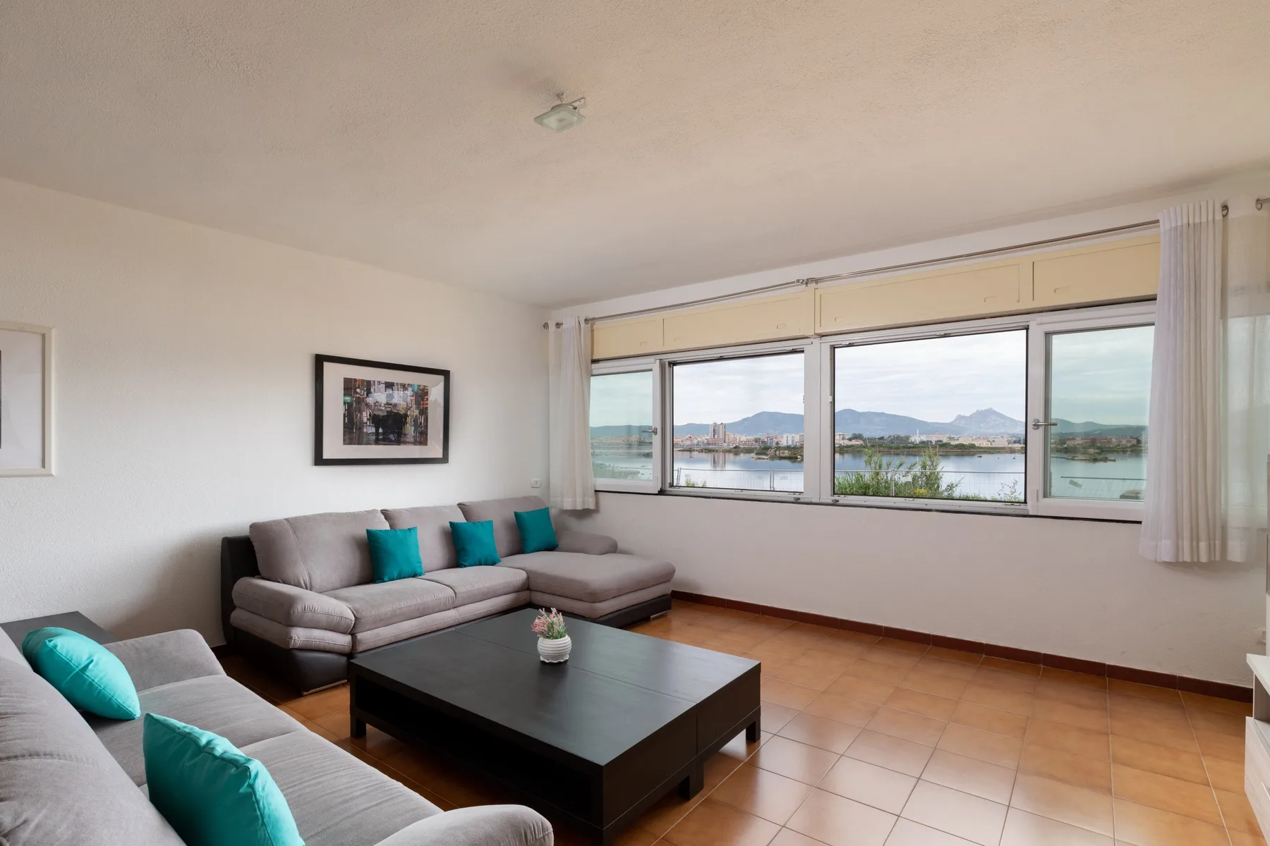 Una sala de estar con asientos y una mesa de centro junto a amplias ventanas con vista al agua.