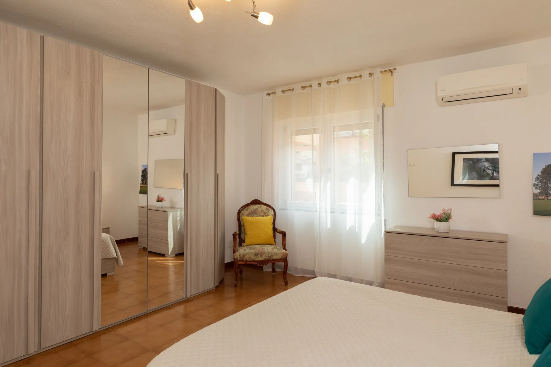 Un dormitorio con un armario grande, una cama y una ventana con cortinas translúcidas.