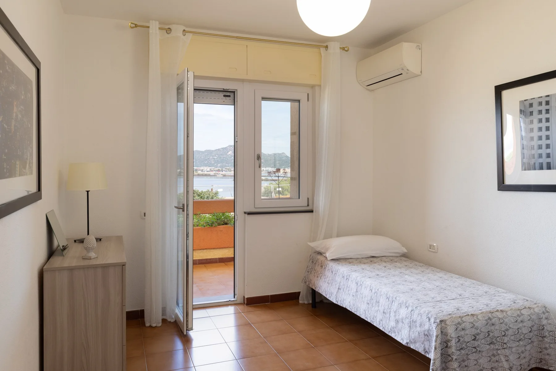 Un dormitorio con una cama individual junto a una puerta abierta al balcón.