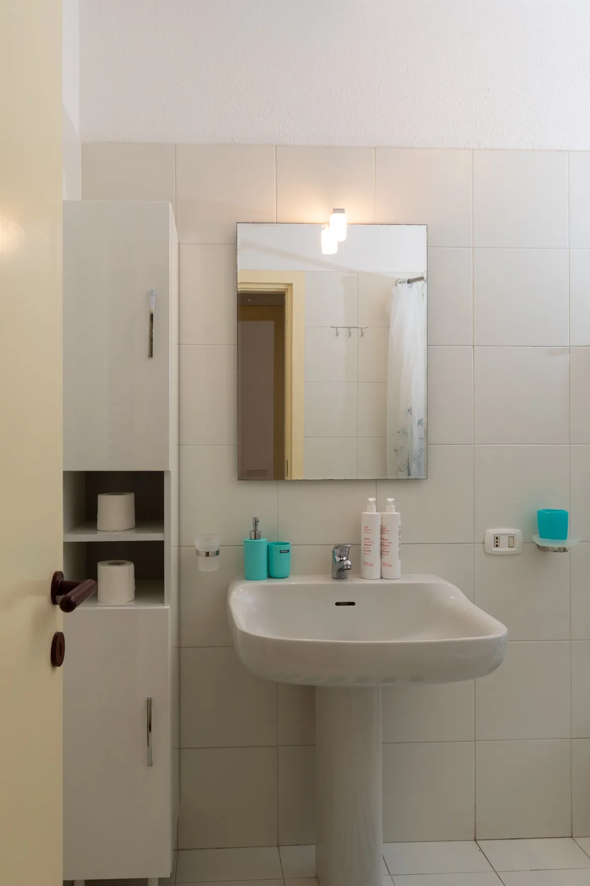 Un baño con azulejos, lavabo suspendido y espejo.