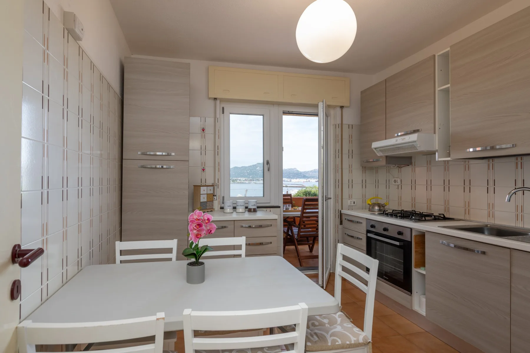 Una cocina luminosa tiene gabinetes claros, una mesa de comedor y una ventana con vista al agua.
