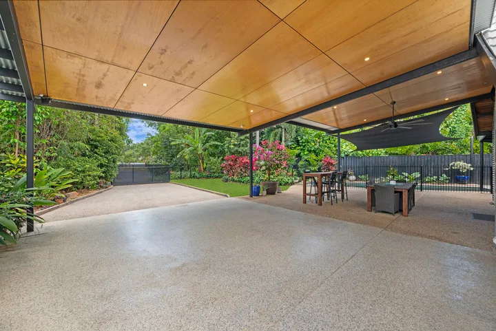 Un patio exterior cubierto con una mesa y asientos junto a un jardín ajardinado.