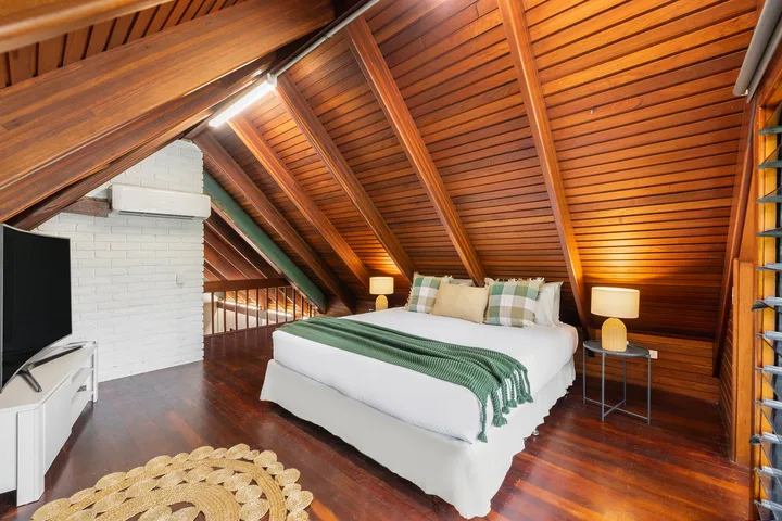 Dormitorio con una cama blanca bajo un techo inclinado de madera.