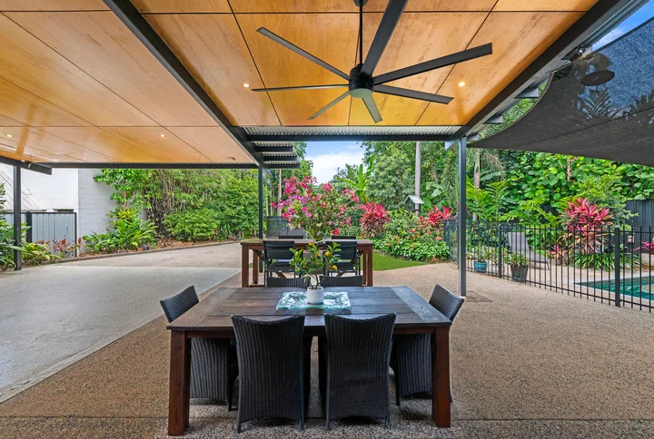 Un comedor al aire libre está bajo un patio cubierto, rodeado de vegetación.