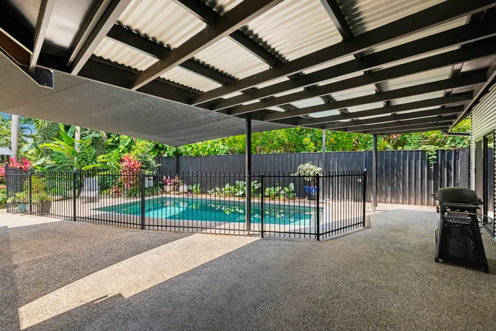 Un patio cubierto da a una piscina rodeada por una cerca negra.