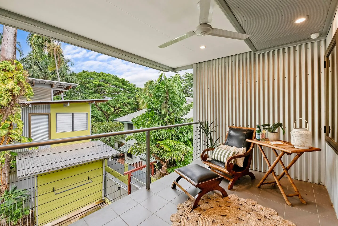 A covered balcony has seating and a small table beside a slatted wall.