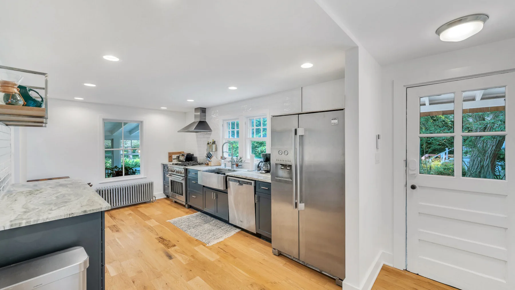 Una cocina luminosa con electrodomésticos de acero inoxidable, suelo de madera y una puerta junto a la vegetación.