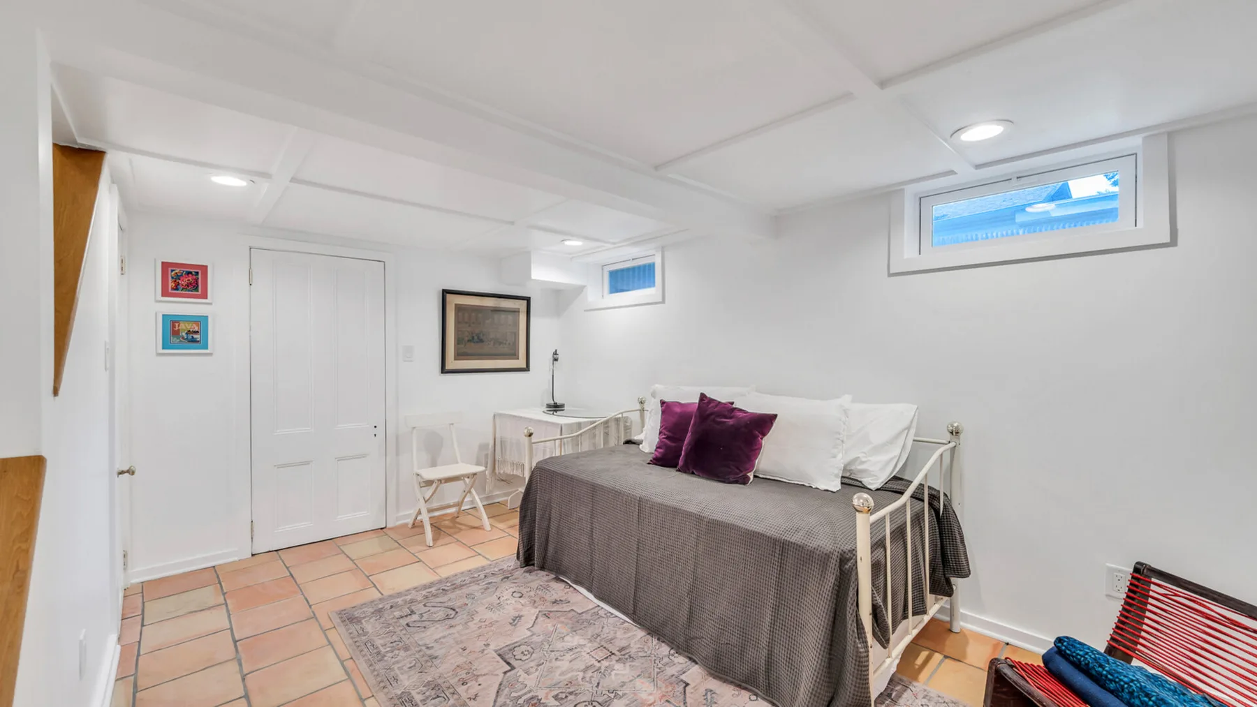 Un dormitorio con una cama vestida con ropa de cama gris y cojines morados.