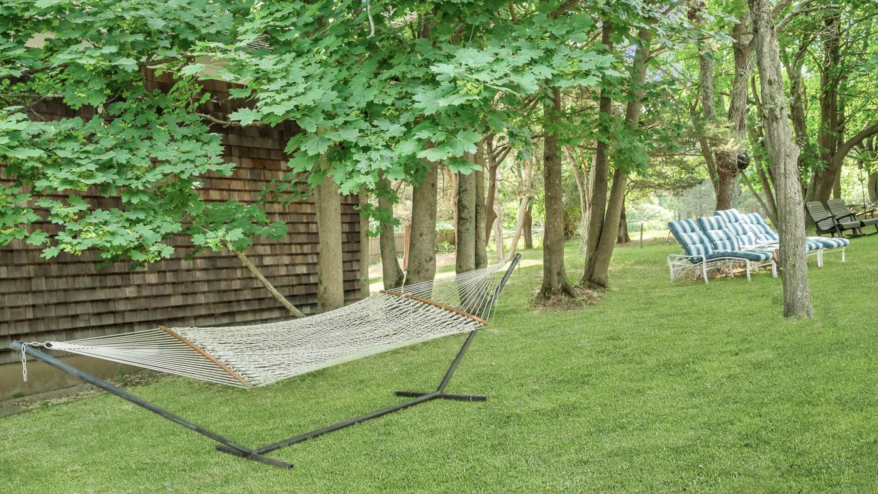 Un patio con césped y sombra de árboles, una hamaca y asientos al aire libre.