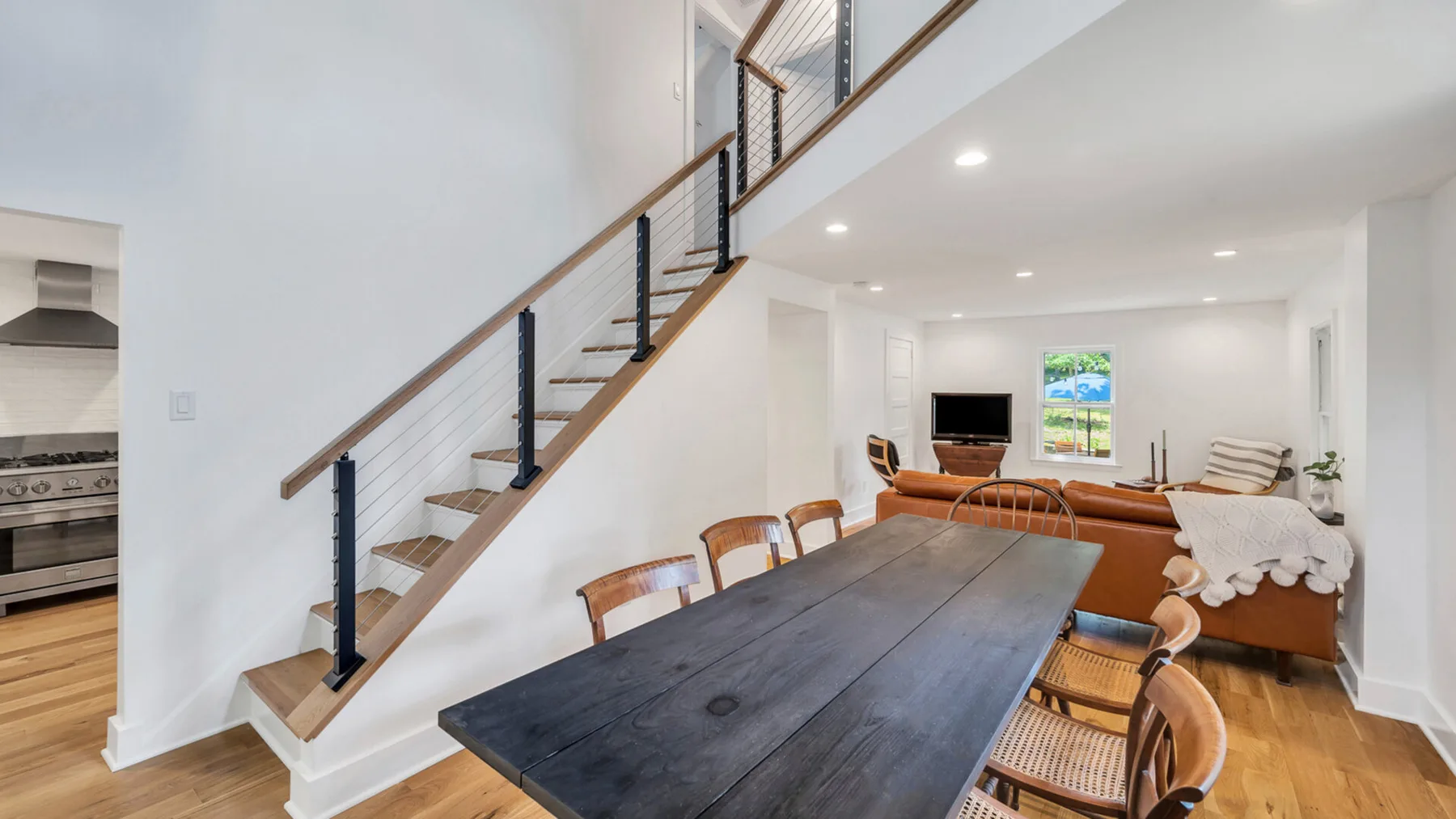 Un comedor con una mesa larga está junto a una sala de estar y una escalera.
