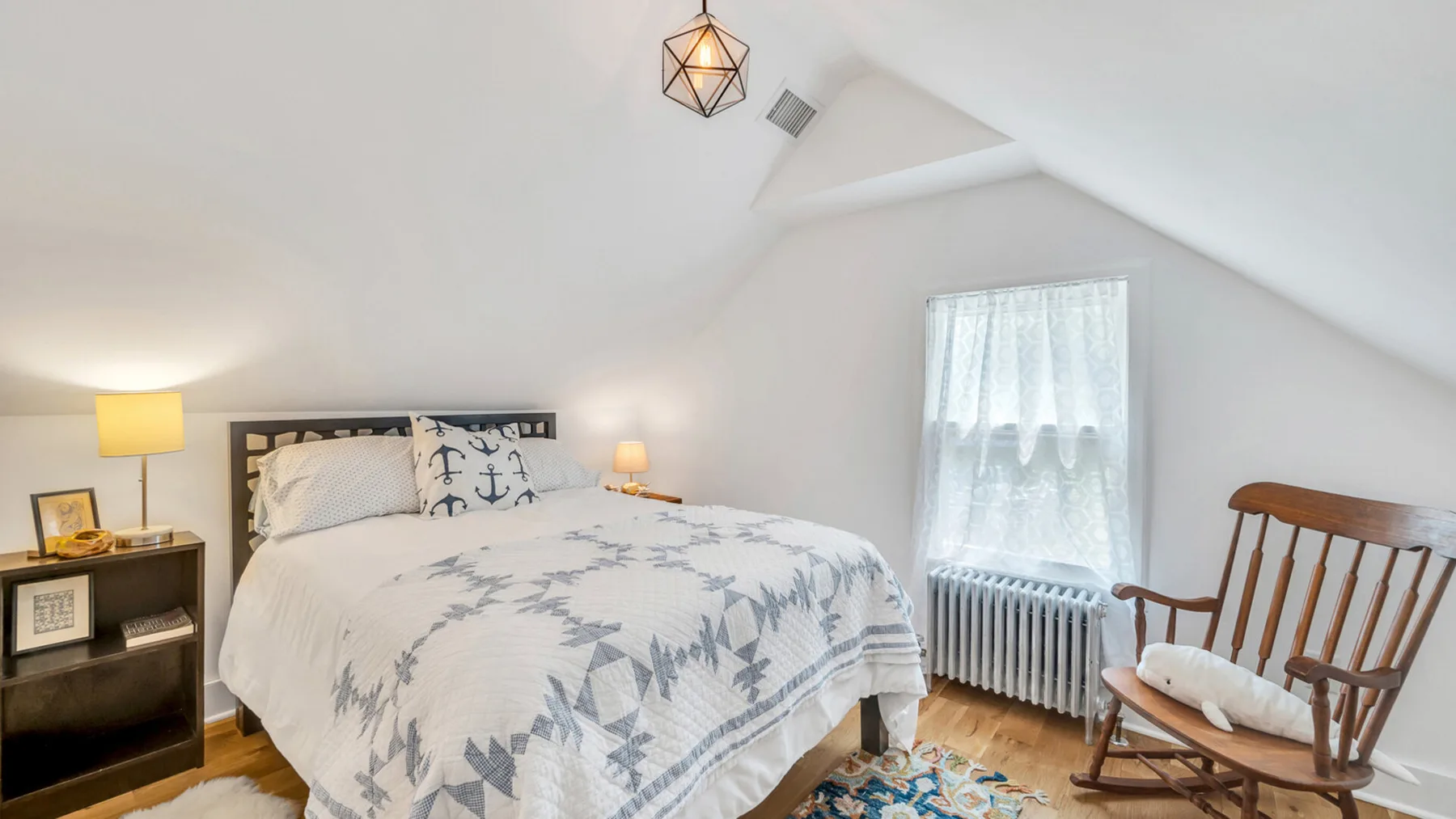 Un dormitorio luminoso con una colcha estampada y una mecedora de madera.