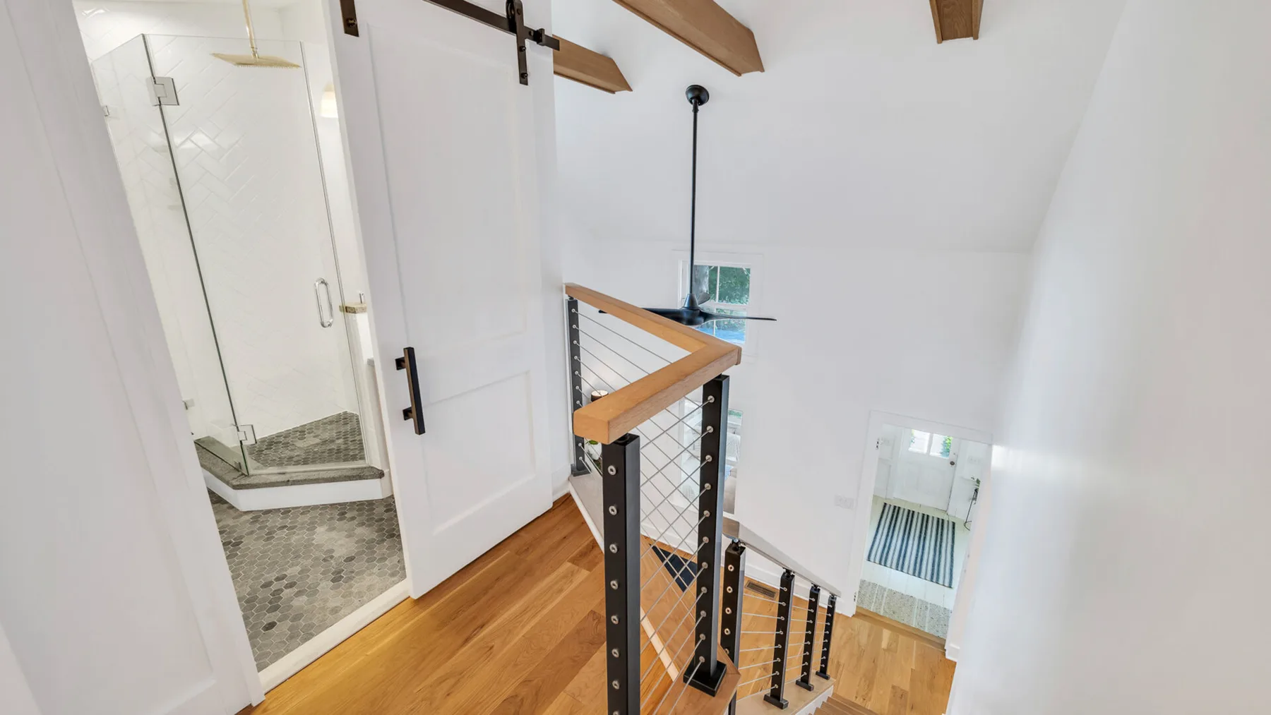 Una escalera luminosa con peldaños de madera, una barandilla y una ducha visible tras una puerta abierta.