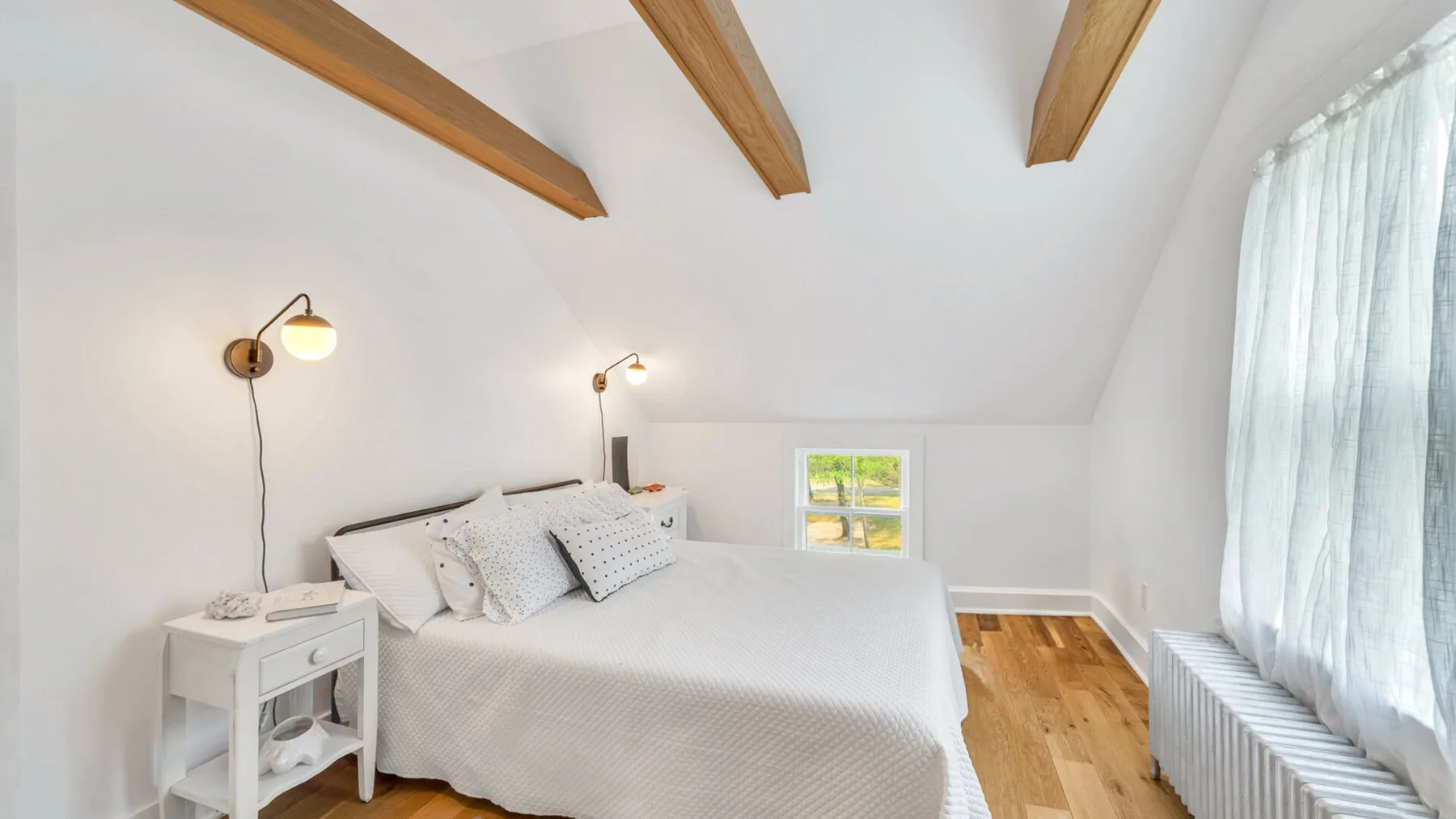 Un dormitorio luminoso con una cama bajo vigas de madera vistas en el techo.