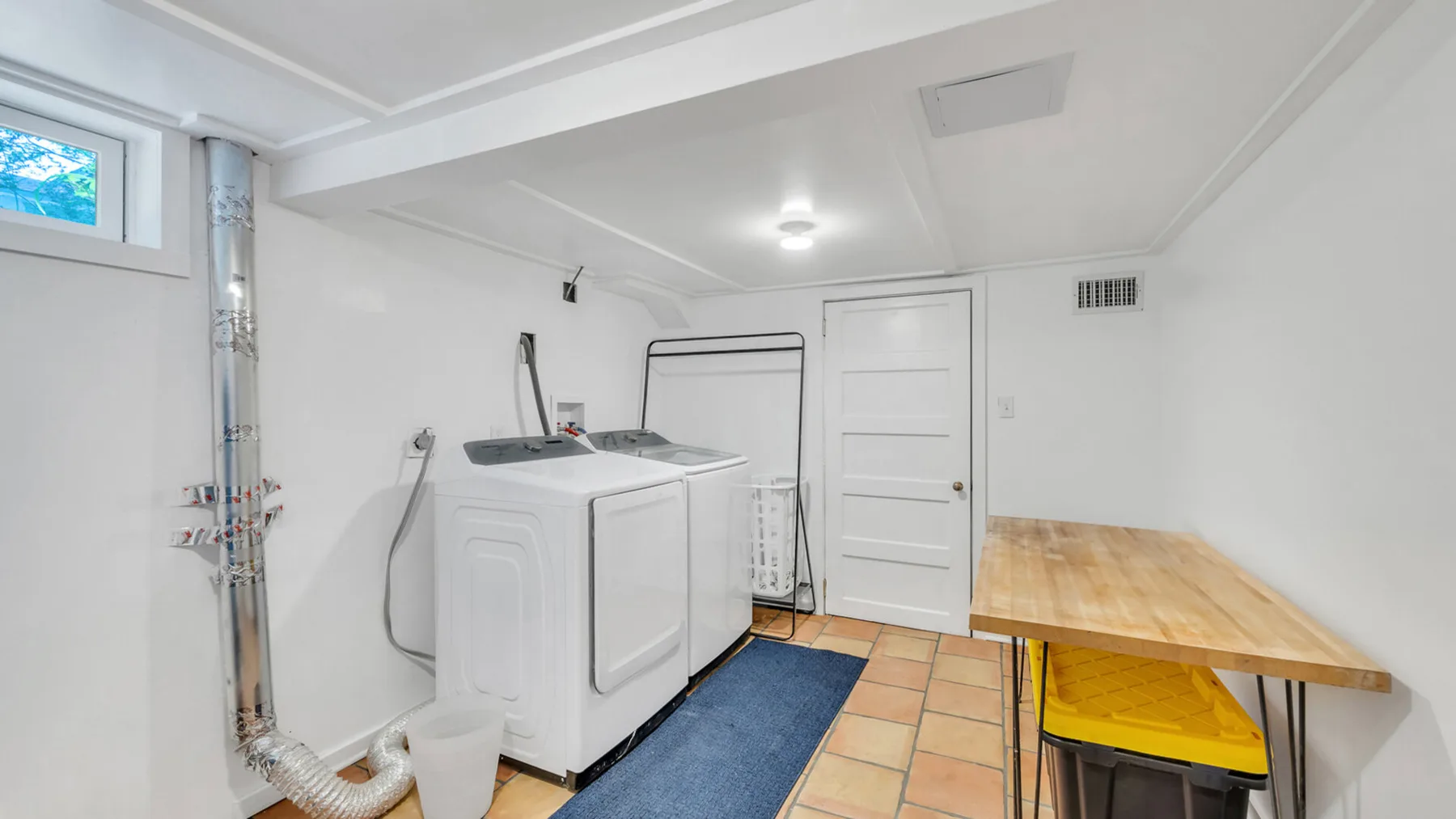Un cuarto de servicio luminoso con máquinas de lavandería y una mesa de madera.