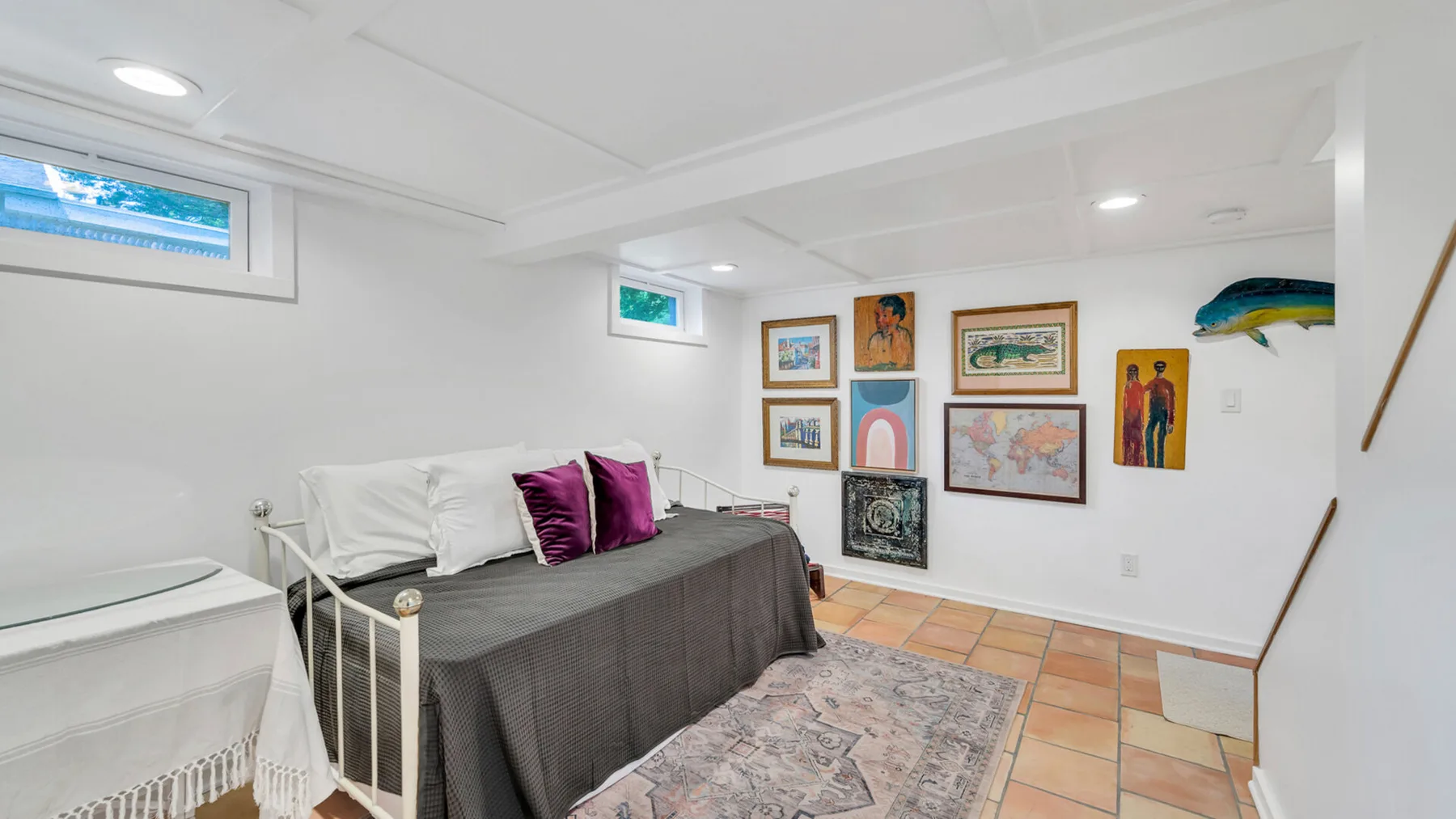 Un dormitorio luminoso con una cama, cuadros enmarcados y una alfombra estampada.