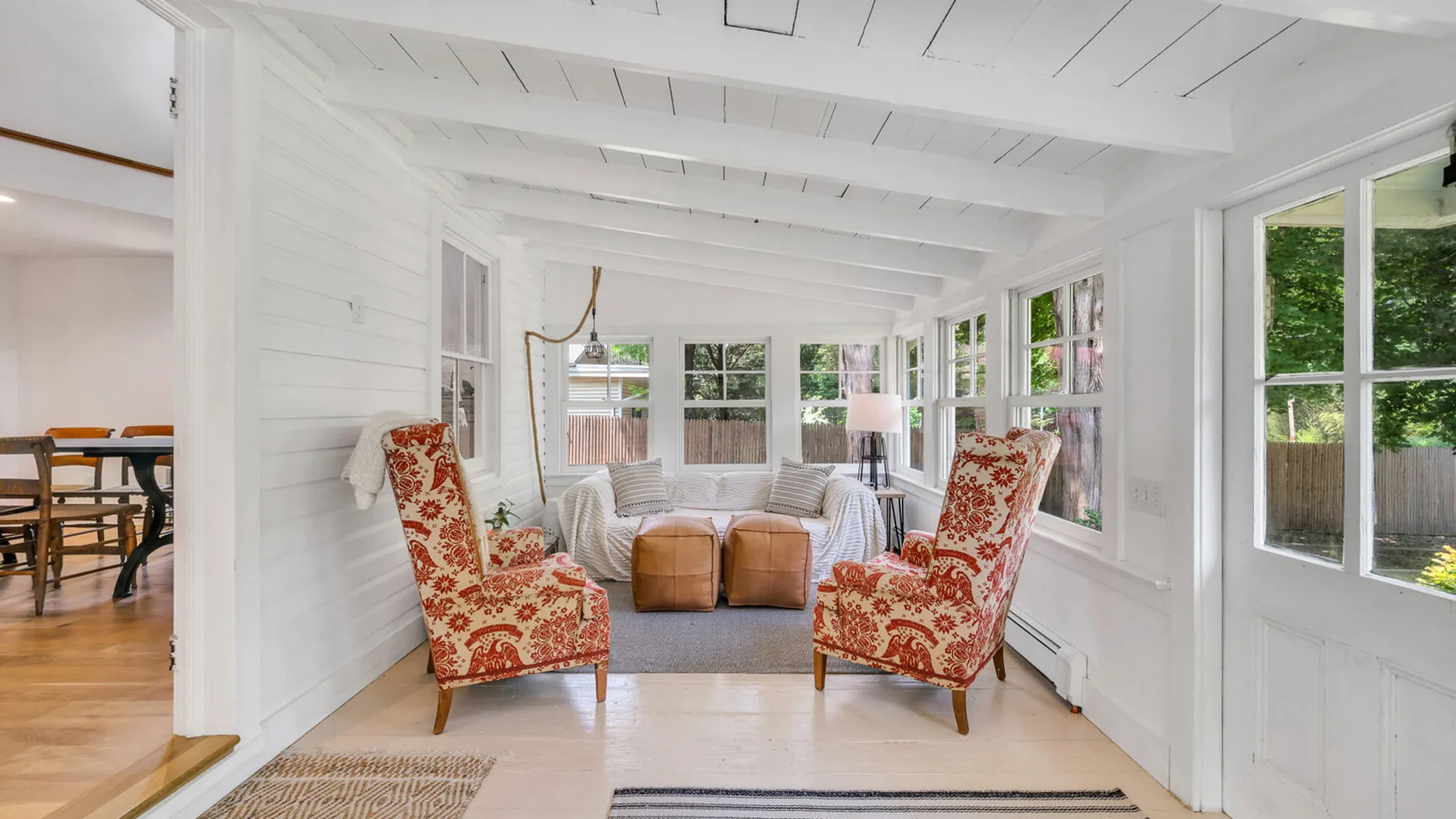 A bright sunroom with patterned seating and large windows overlooking greenery.