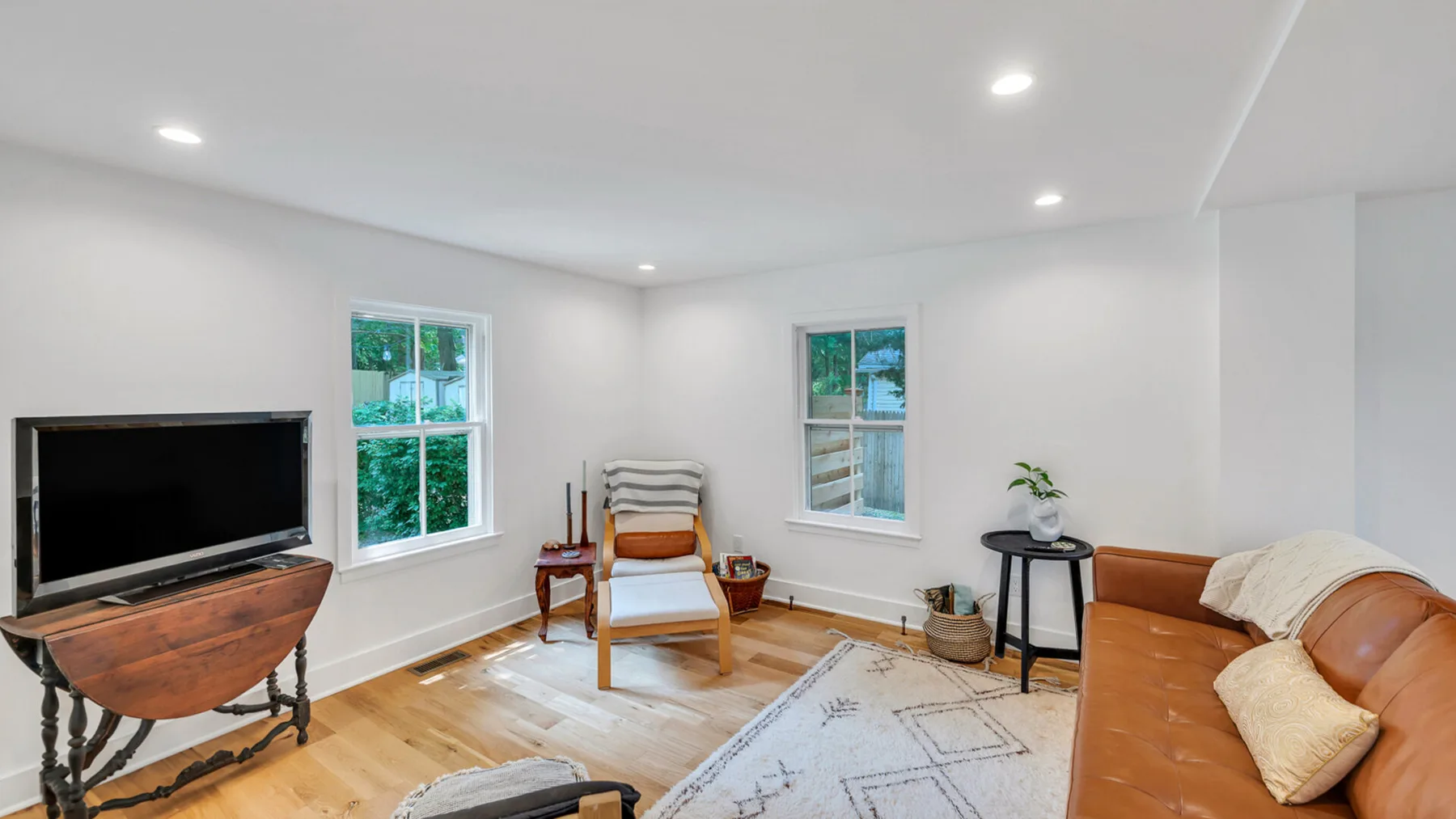 Una sala luminosa con asientos, un televisor y ventanas con vista a la vegetación.
