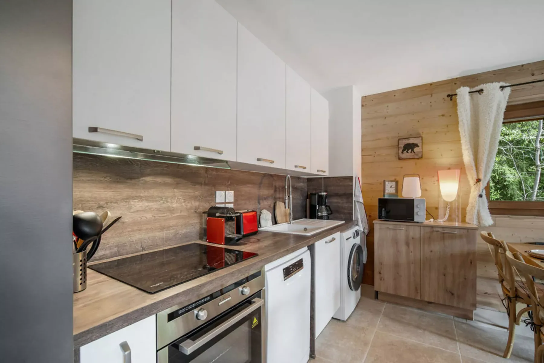 A kitchen with white cabinetry, a cooktop, and a dining area by the window.