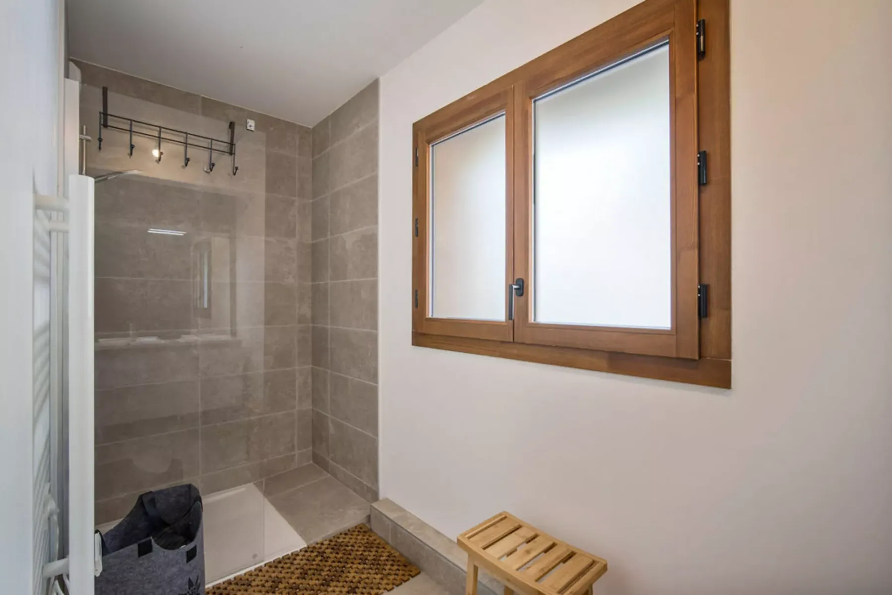 A tiled bathroom with a glass shower area and a wooden-framed window.