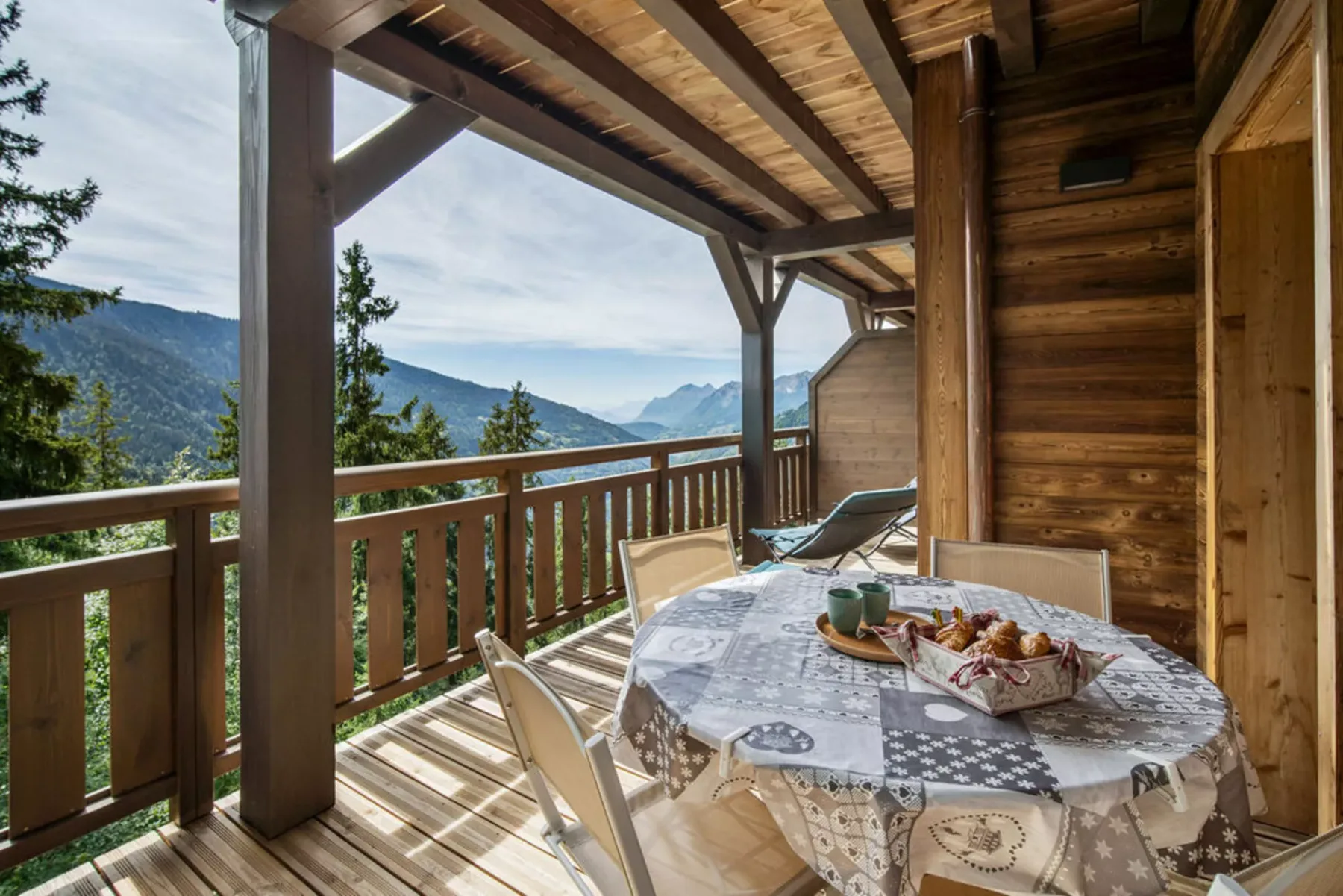 A covered wooden deck has a dining table and mountain views.