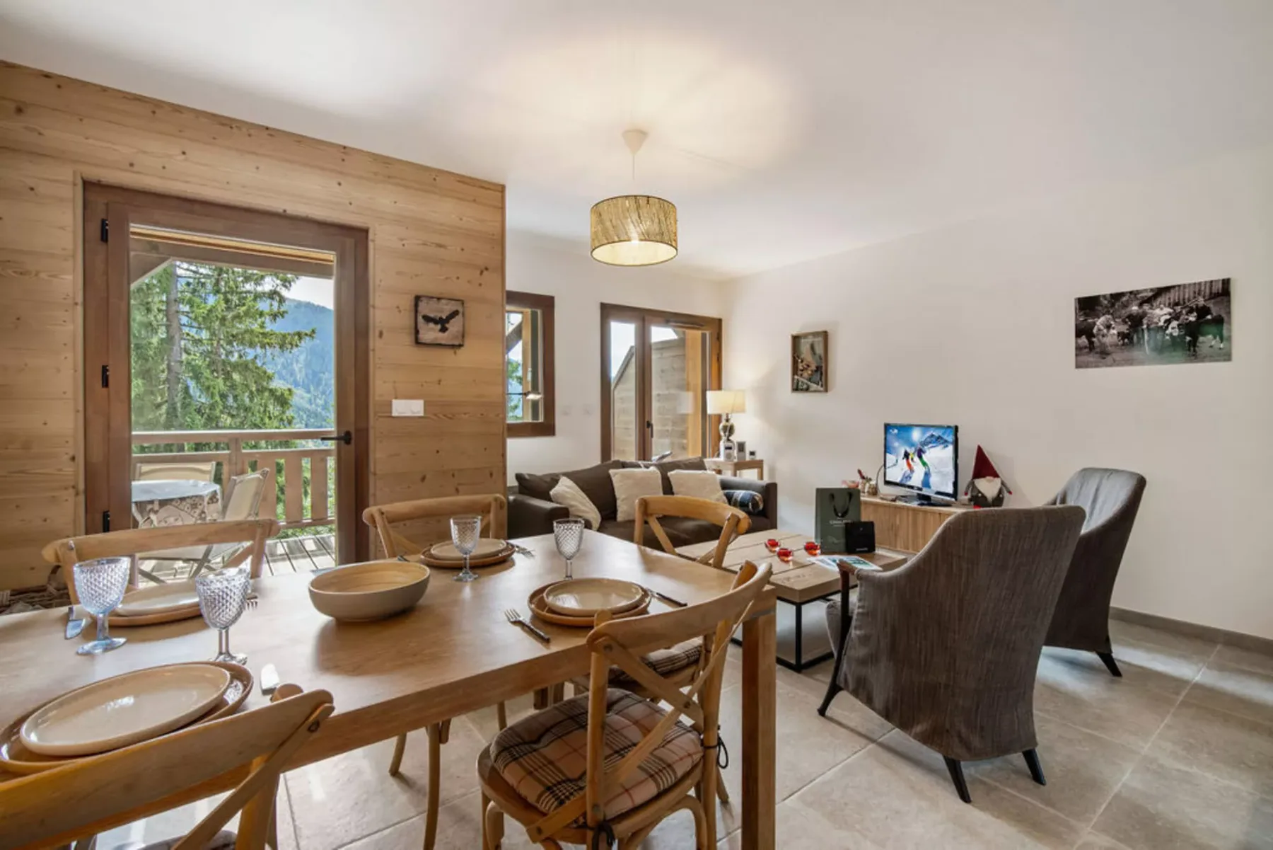 A dining and living area with a wooden table and seating beside a balcony door.