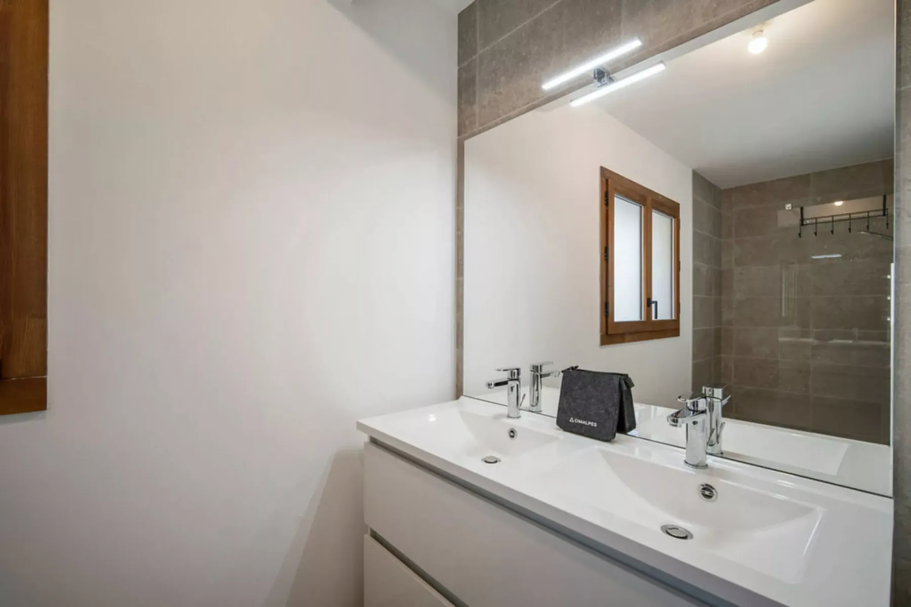 A bathroom vanity with a wide mirror and a shower visible in the reflection.
