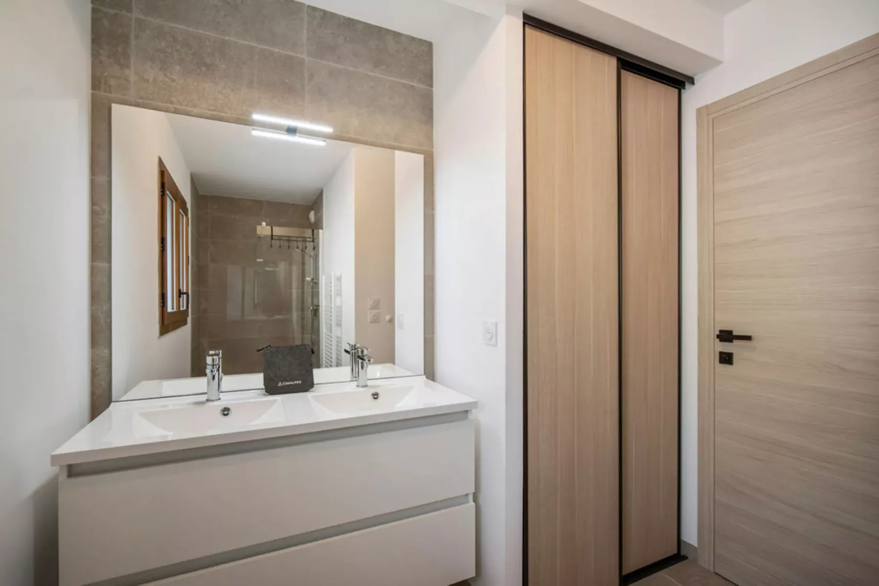 A bathroom vanity with a wide mirror and light wood cabinetry.