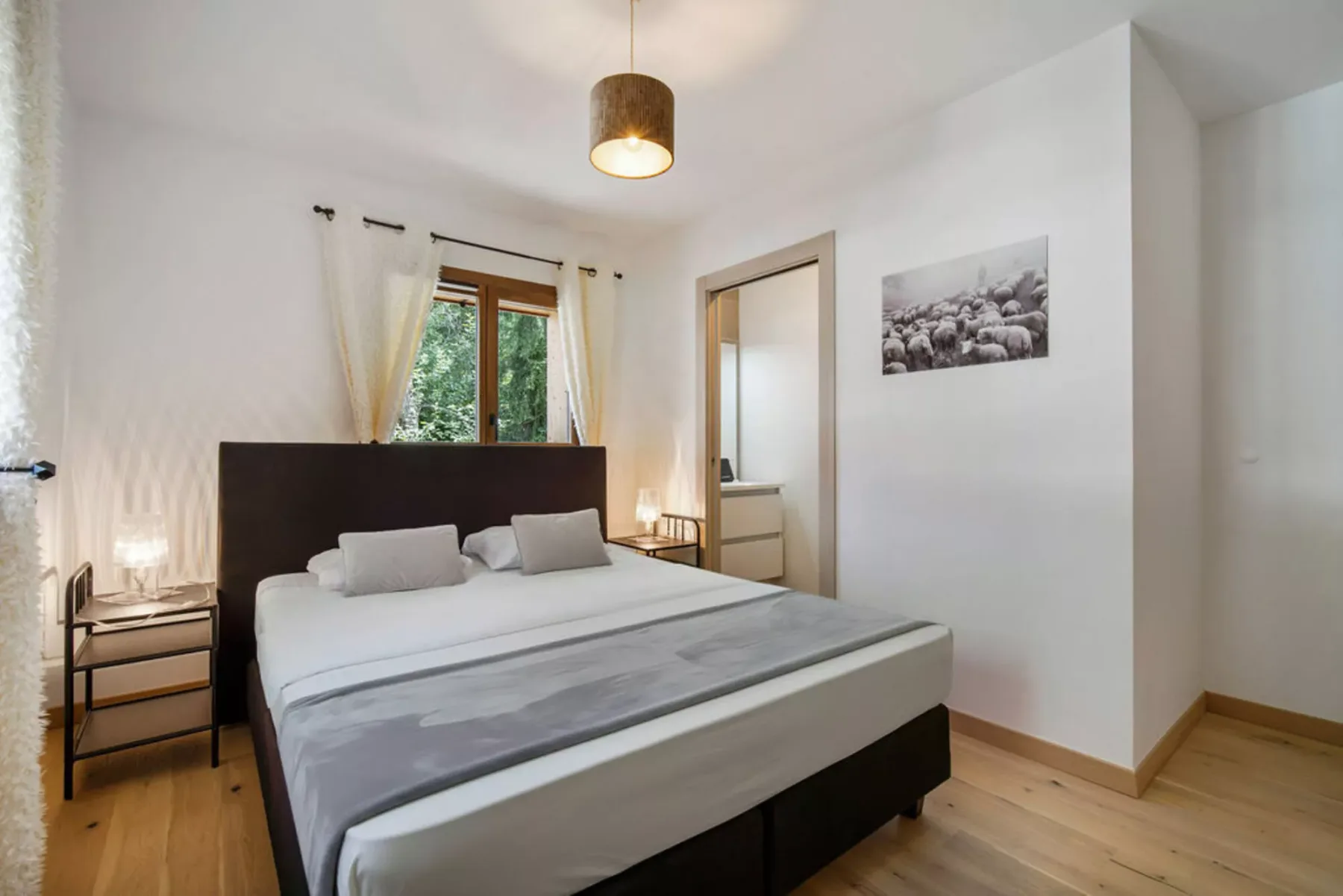 A bright bedroom with a bed beneath a window and framed wall art.