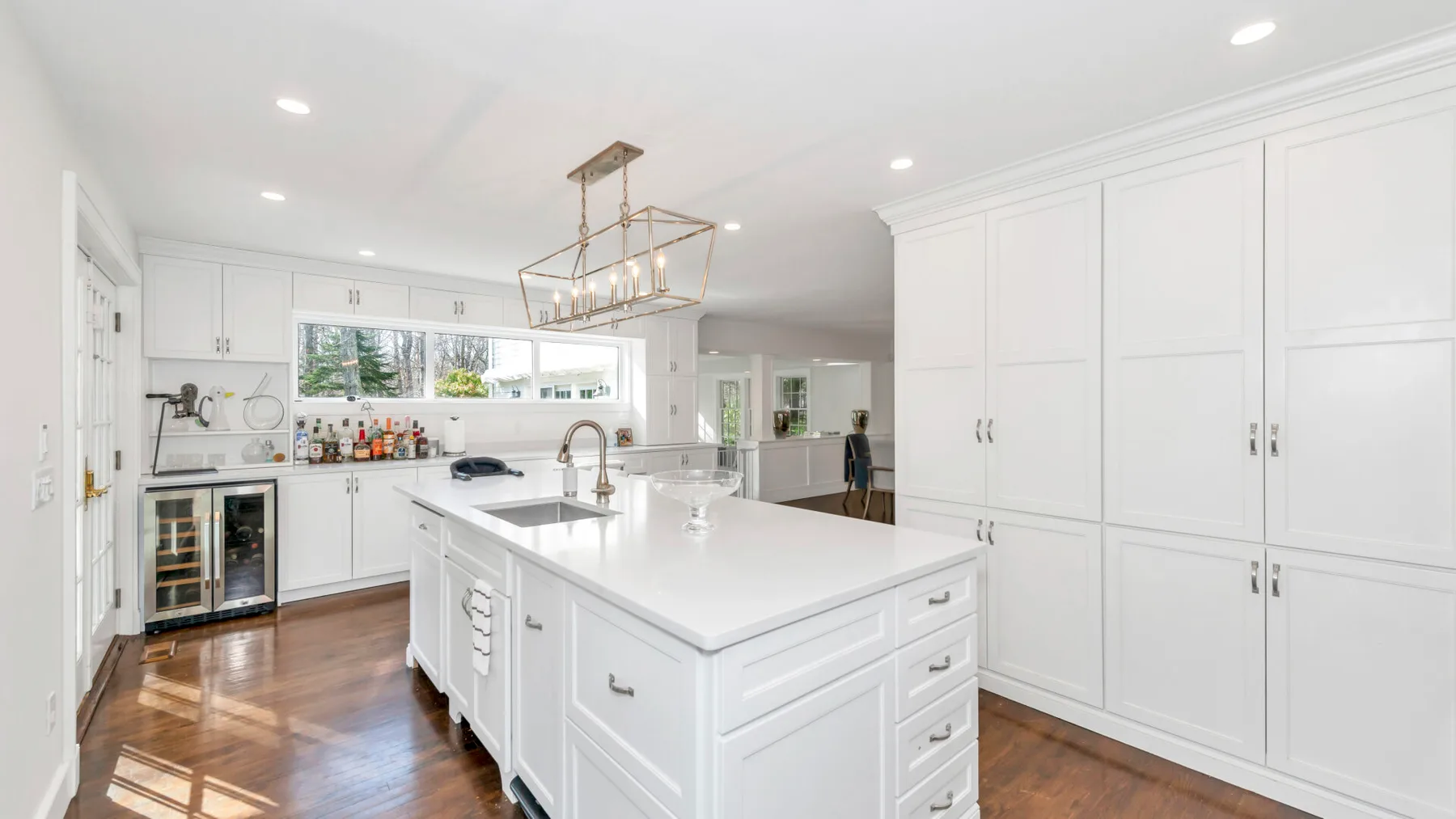 Una cocina blanca y luminosa con una gran isla y piso de madera.