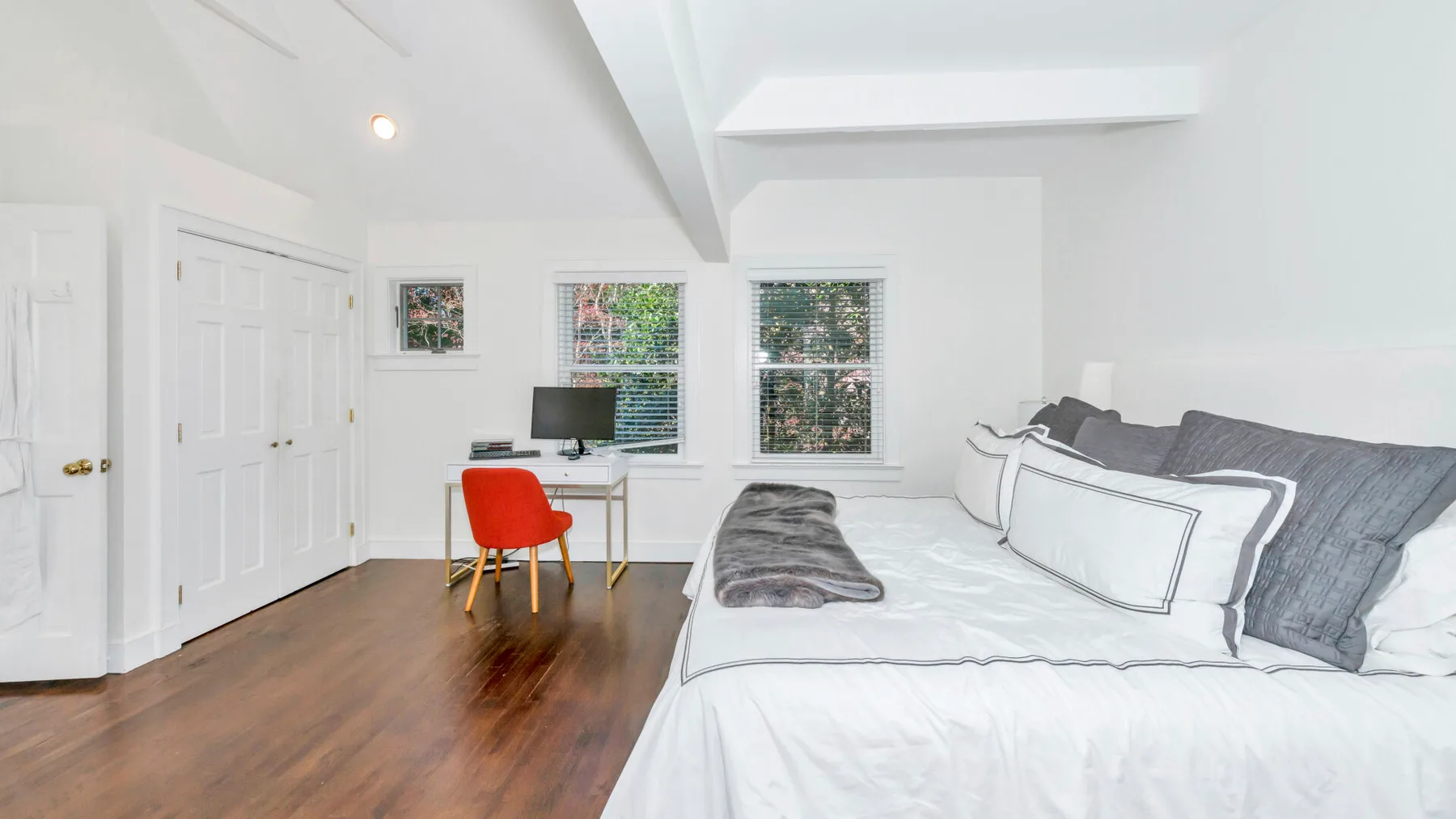 Un dormitorio luminoso tiene una cama grande, un escritorio y ventanas.