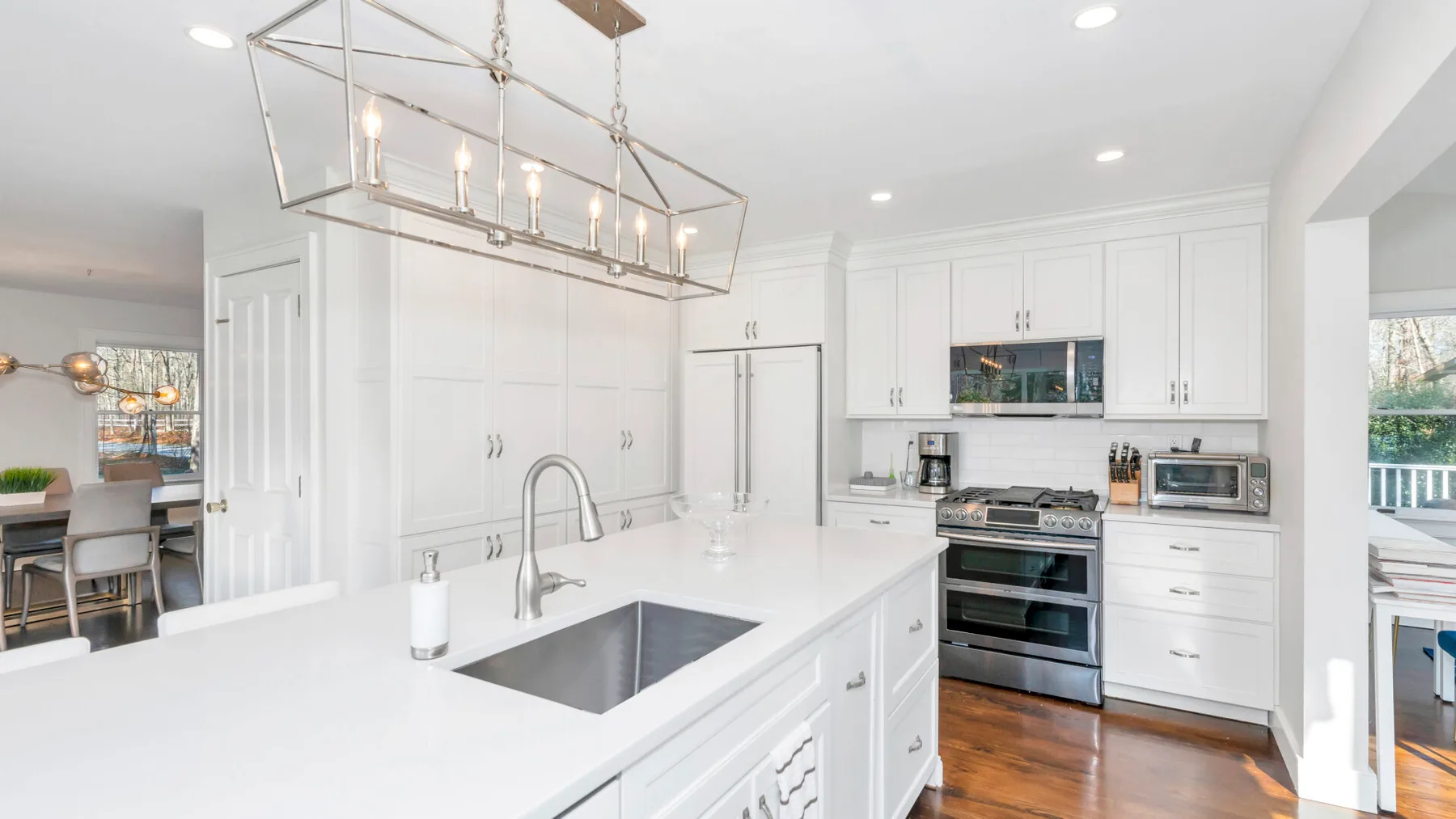 Una cocina blanca y luminosa con isla central, fregadero y electrodomésticos de acero inoxidable.