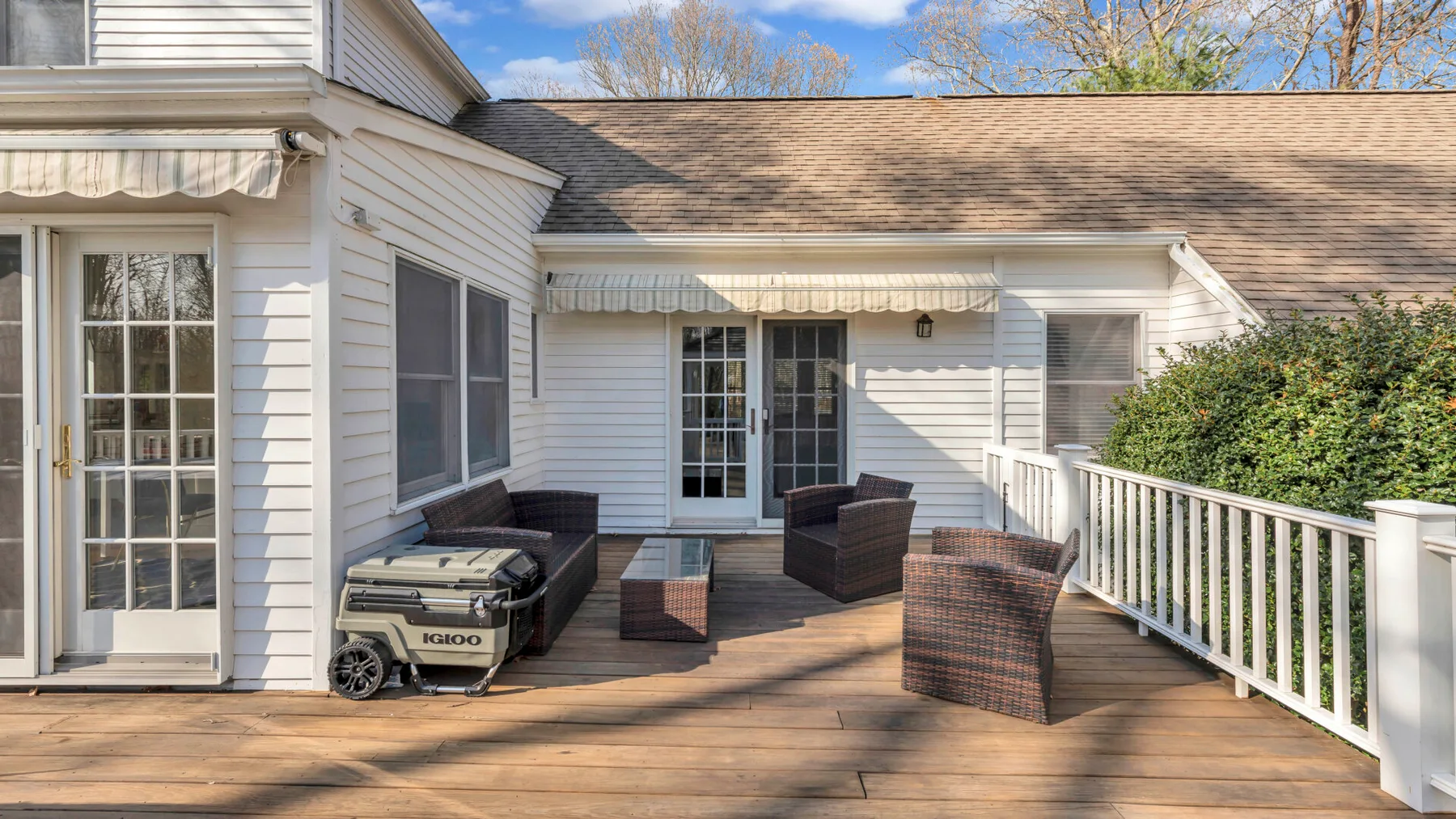 Una terraza exterior de madera con asientos y una parrilla junto a una casa blanca.