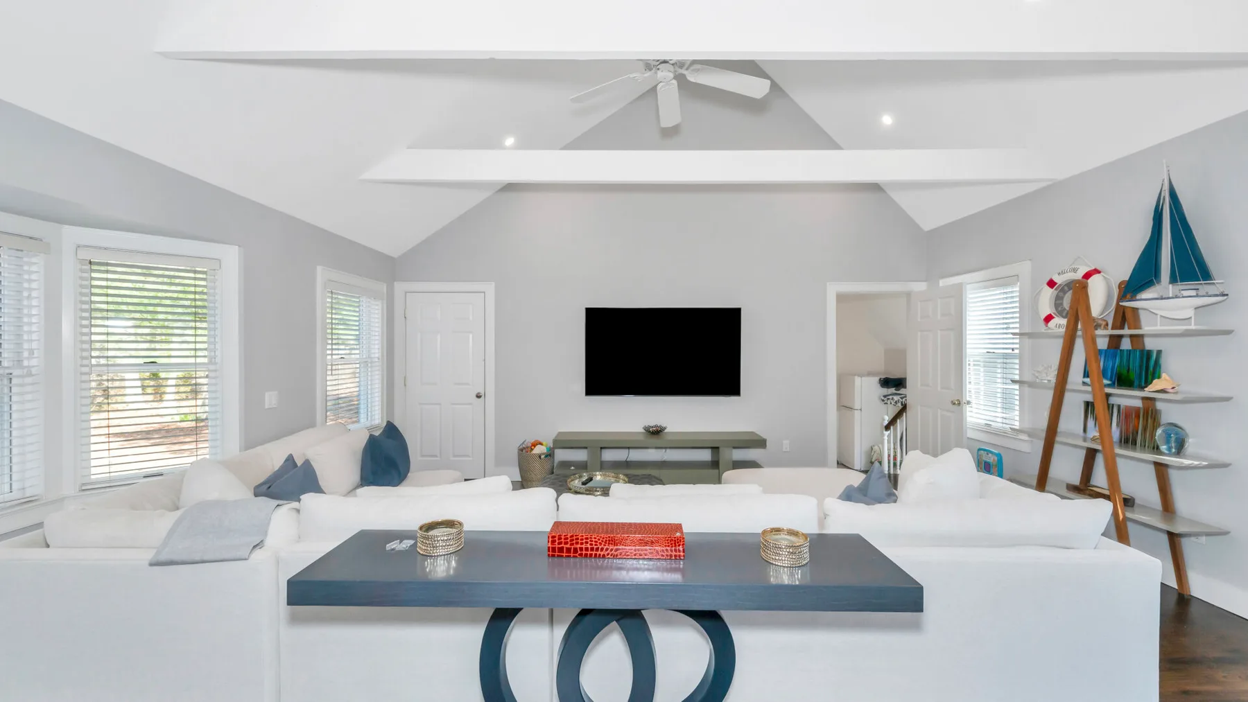 Una sala luminosa con asientos blancos, un televisor en la pared y una mesa de centro.