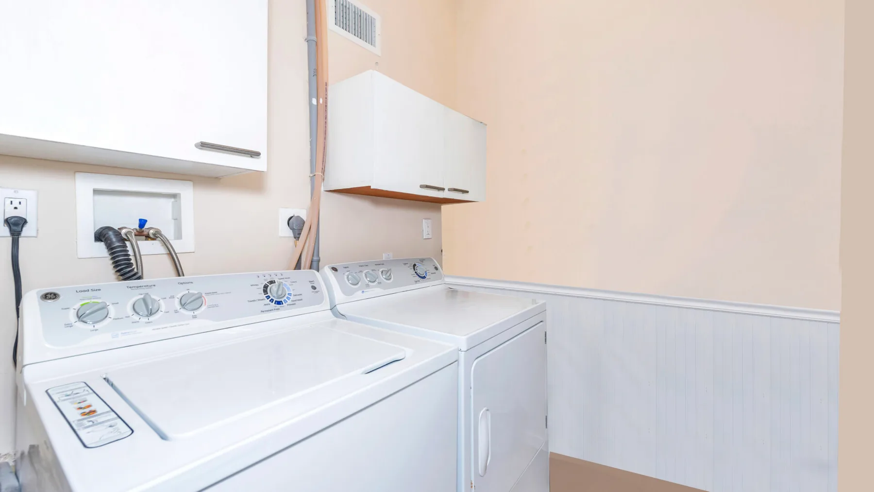 Zona de lavandería con lavadora y secadora debajo de armarios de pared.