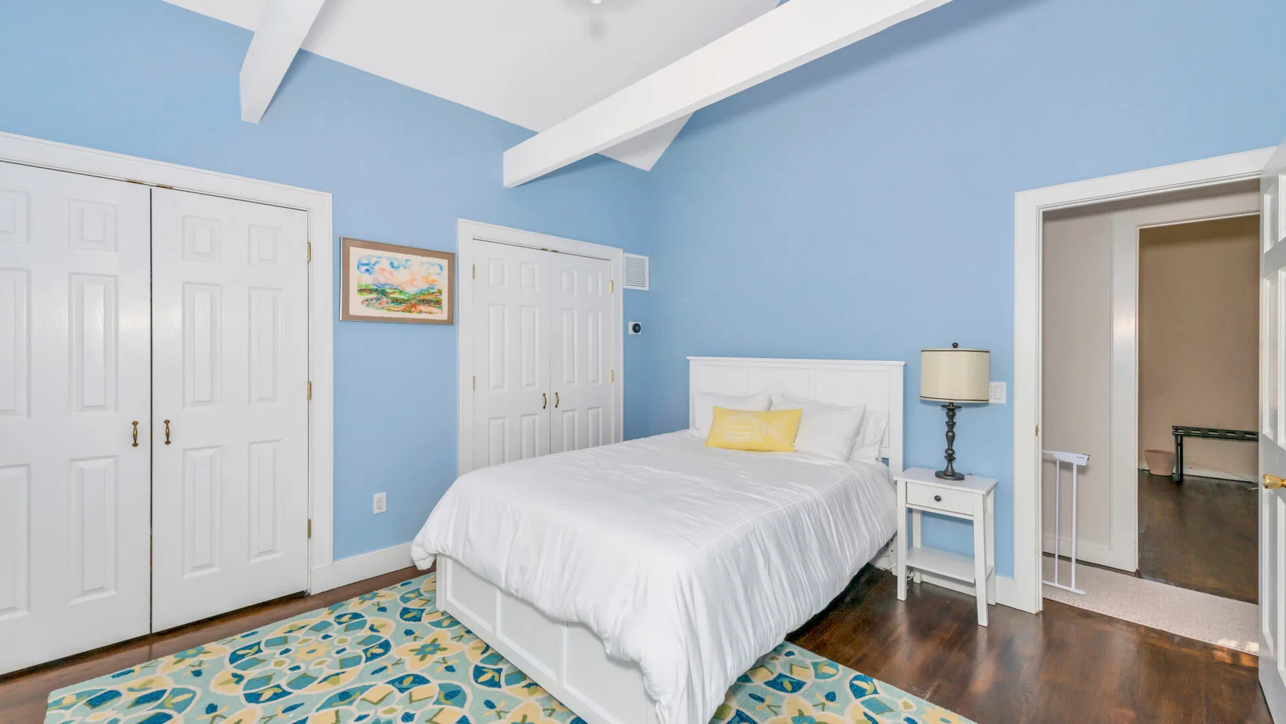 Un dormitorio con una cama blanca, paredes azules y una alfombra estampada.