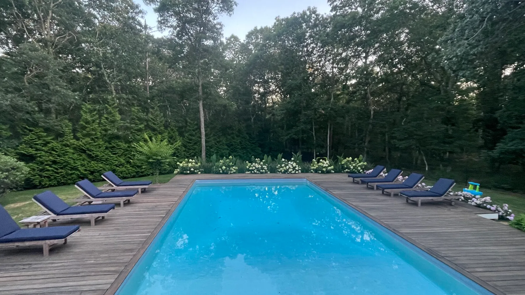 Una piscina al aire libre está sobre una terraza de madera rodeada de árboles.