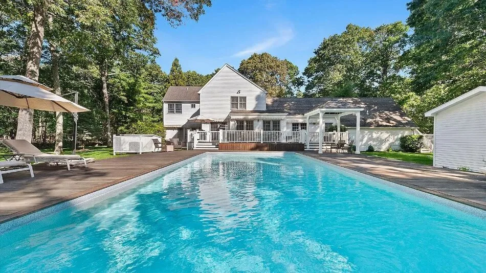 Piscina al aire libre junto a una casa grande y una terraza de madera.