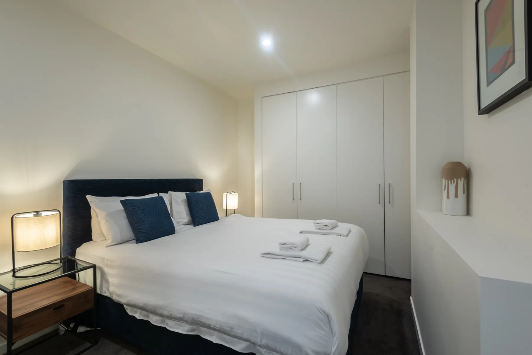 A bedroom with a neatly made bed and a large white wardrobe.