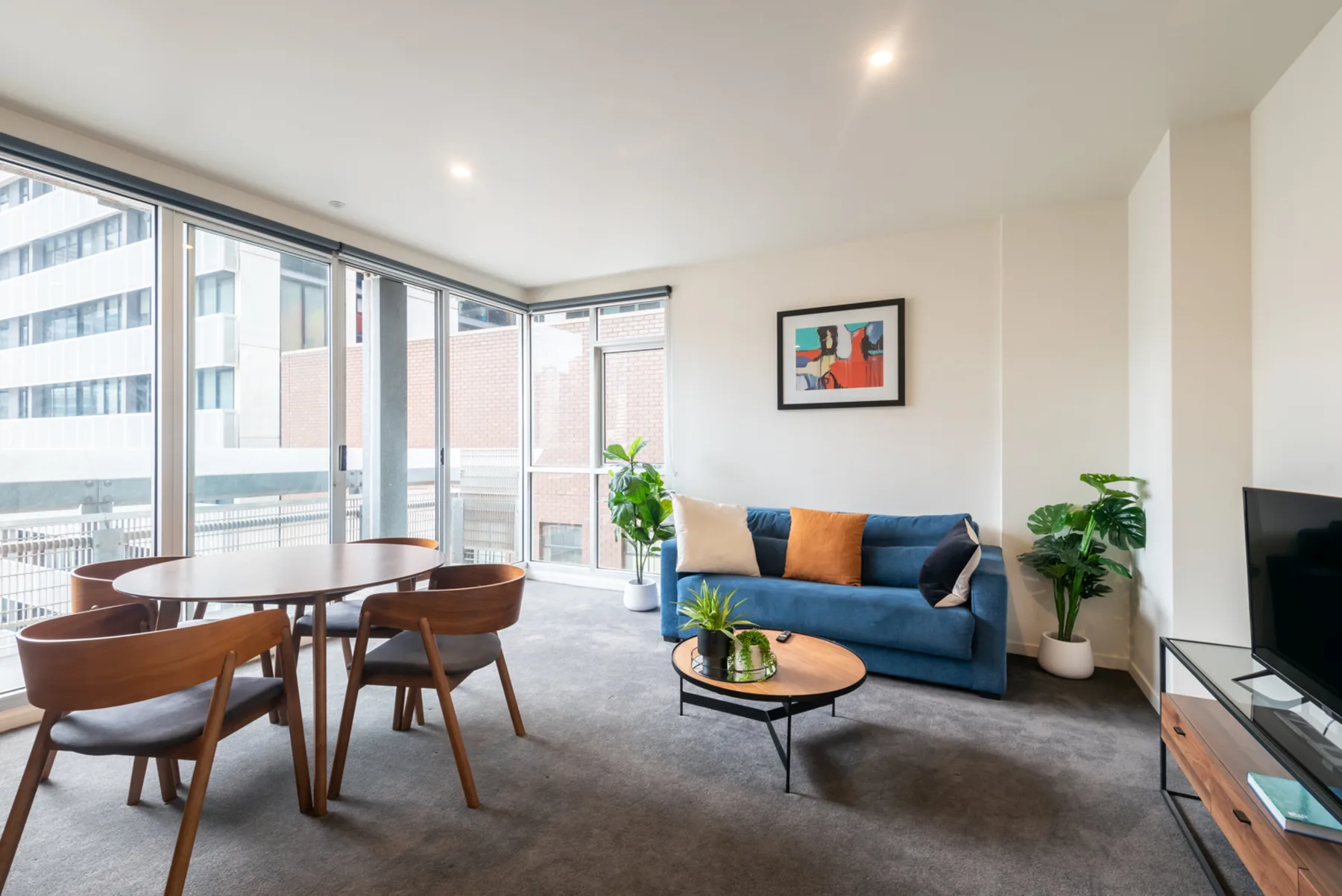 A bright living room with a blue sofa and dining table beside large windows.