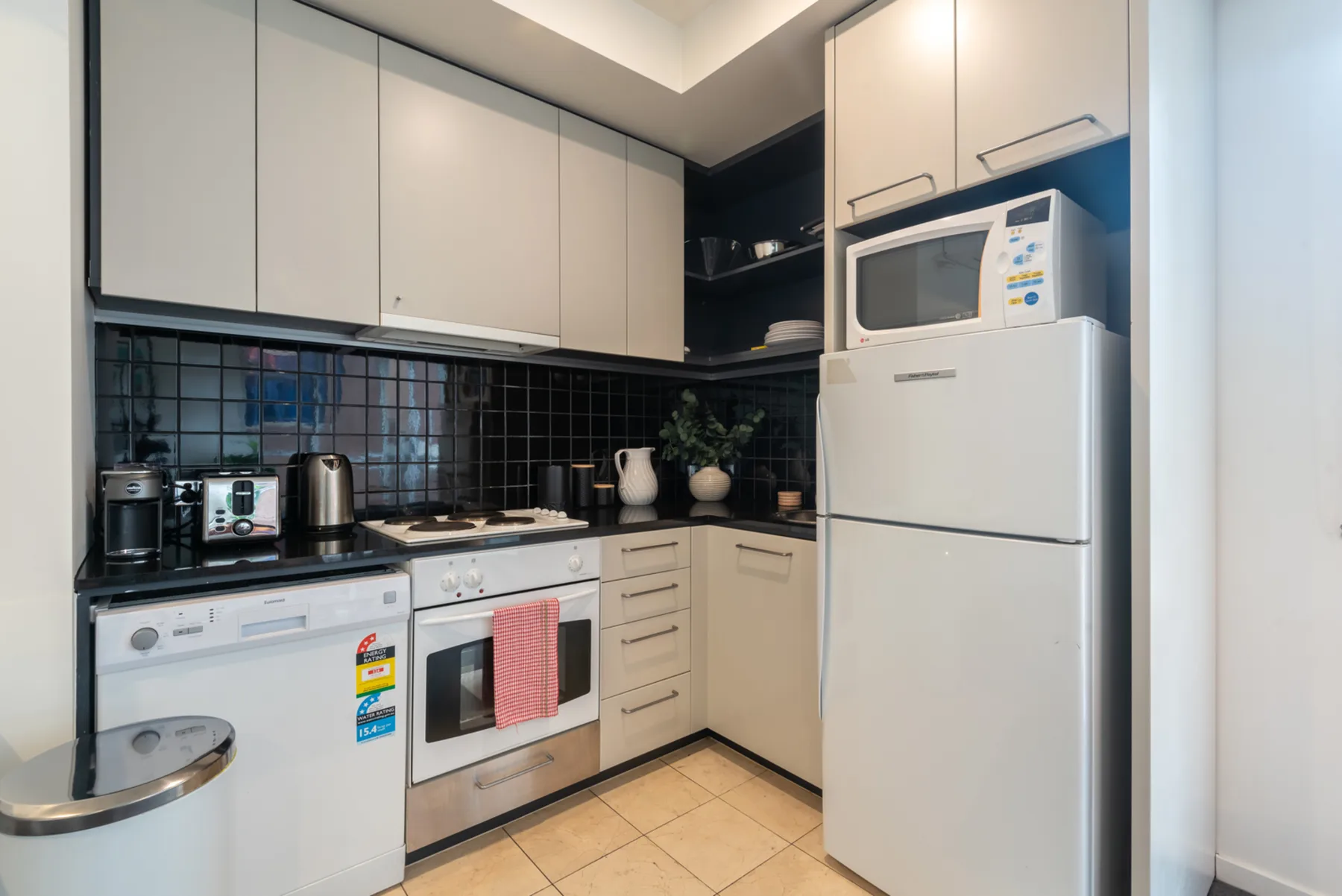 A compact kitchen with light cabinets and a black tiled backsplash.