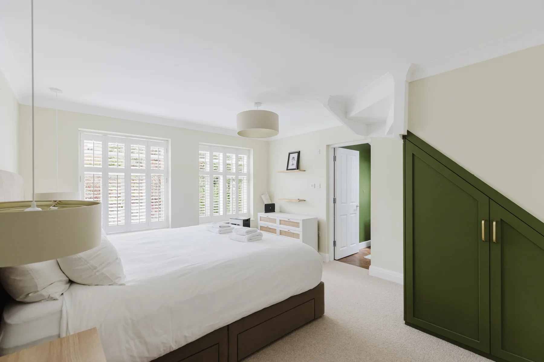 A bright bedroom with a large bed, shuttered windows, and a green wardrobe.