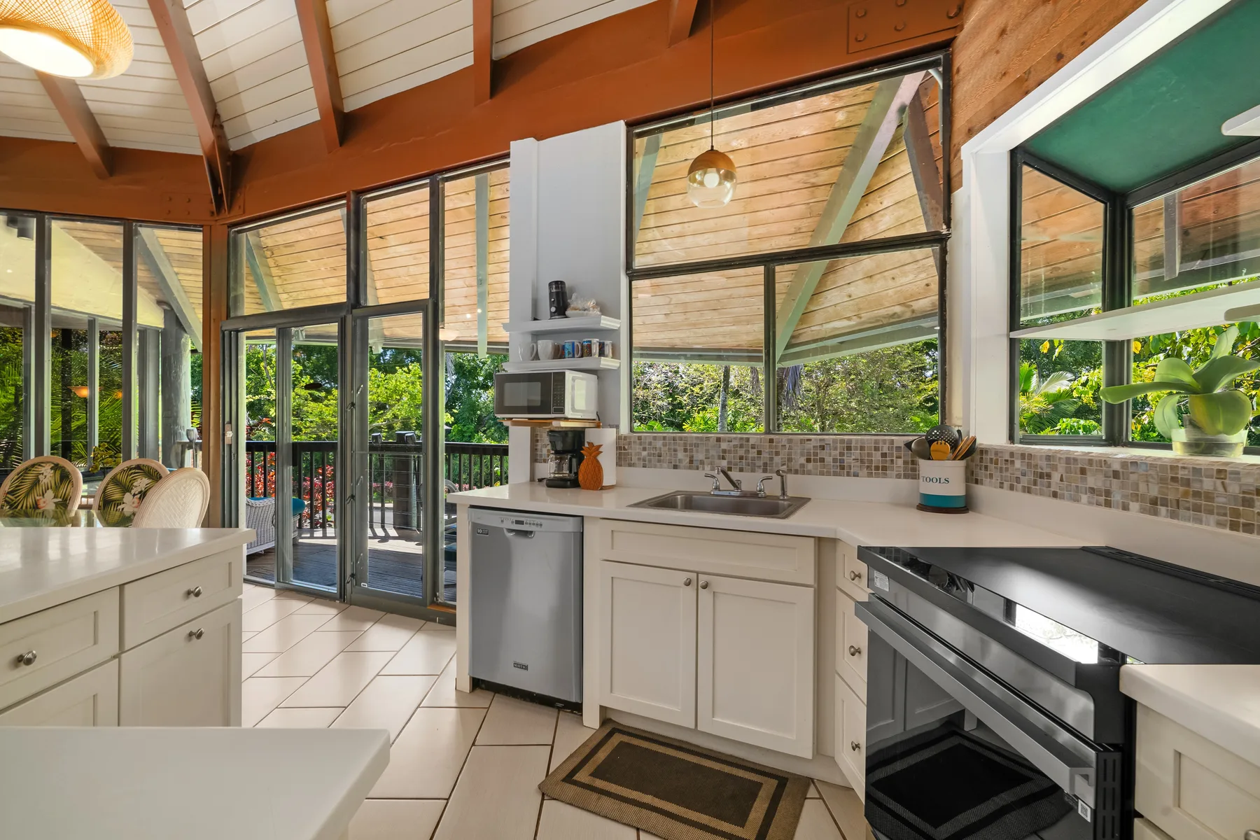 A bright kitchen with white cabinets, a sink, and large windows overlooking greenery.