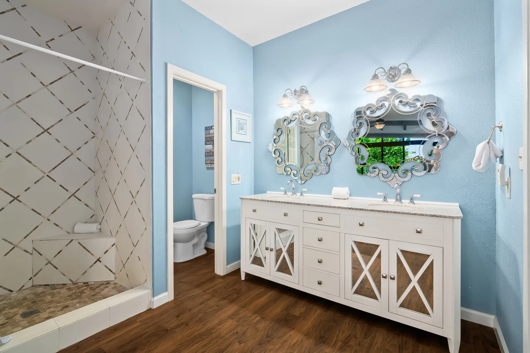 A blue bathroom with a long vanity, ornate mirrors, and a glass shower.