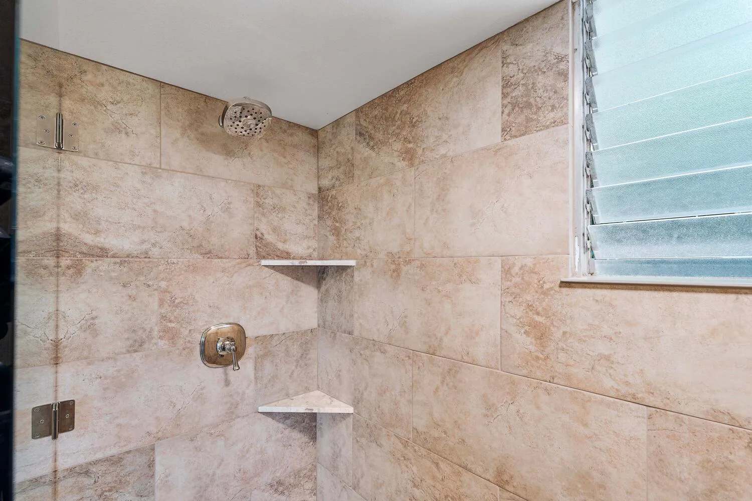Una zona de ducha con azulejos, un cabezal montado en la pared y estantes esquineros.