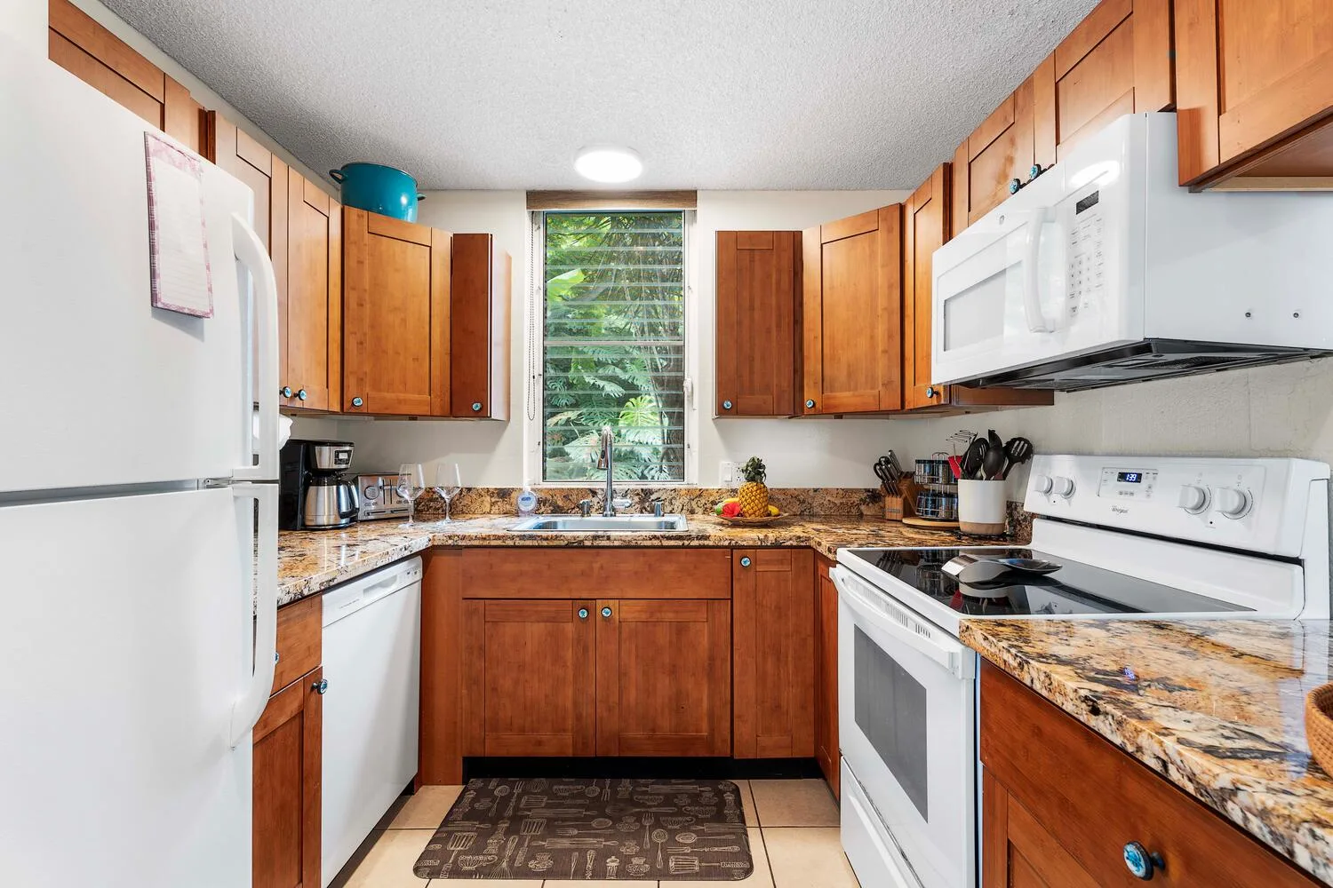 Una cocina con armarios de madera, una ventana central y electrodomésticos junto a las encimeras.